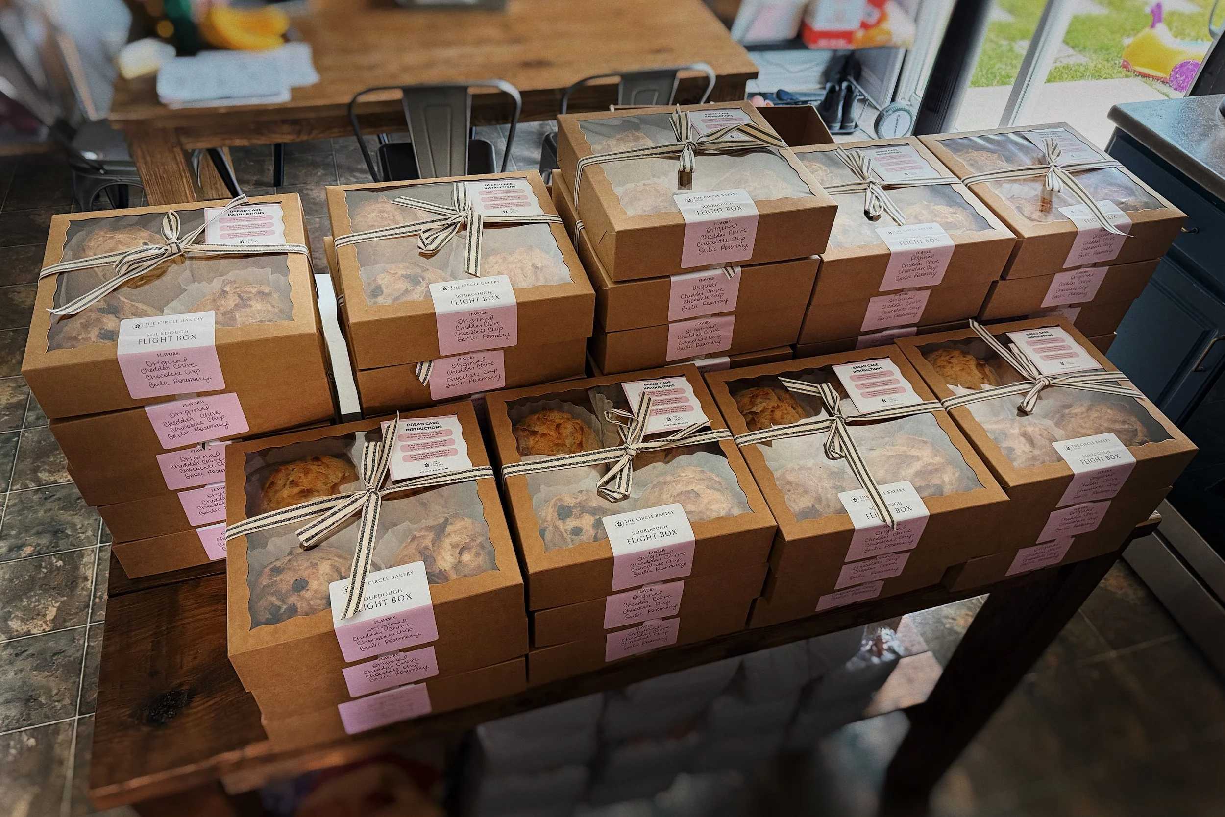 A table filled with boxes of baked goods labeled 'Sourdough Flight Box' from The Circle Bakery, with visible cookies inside some of the boxes.