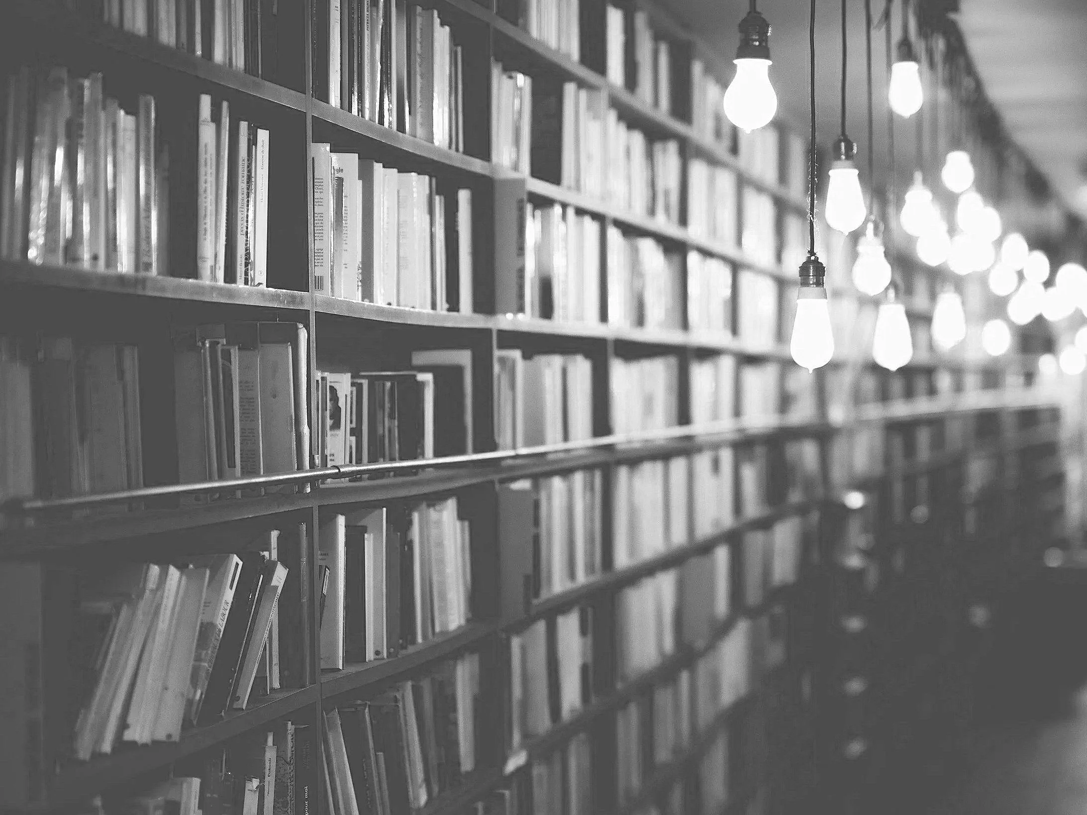 Black and white photo of a bookshelf filled with books and hanging light bulbs.