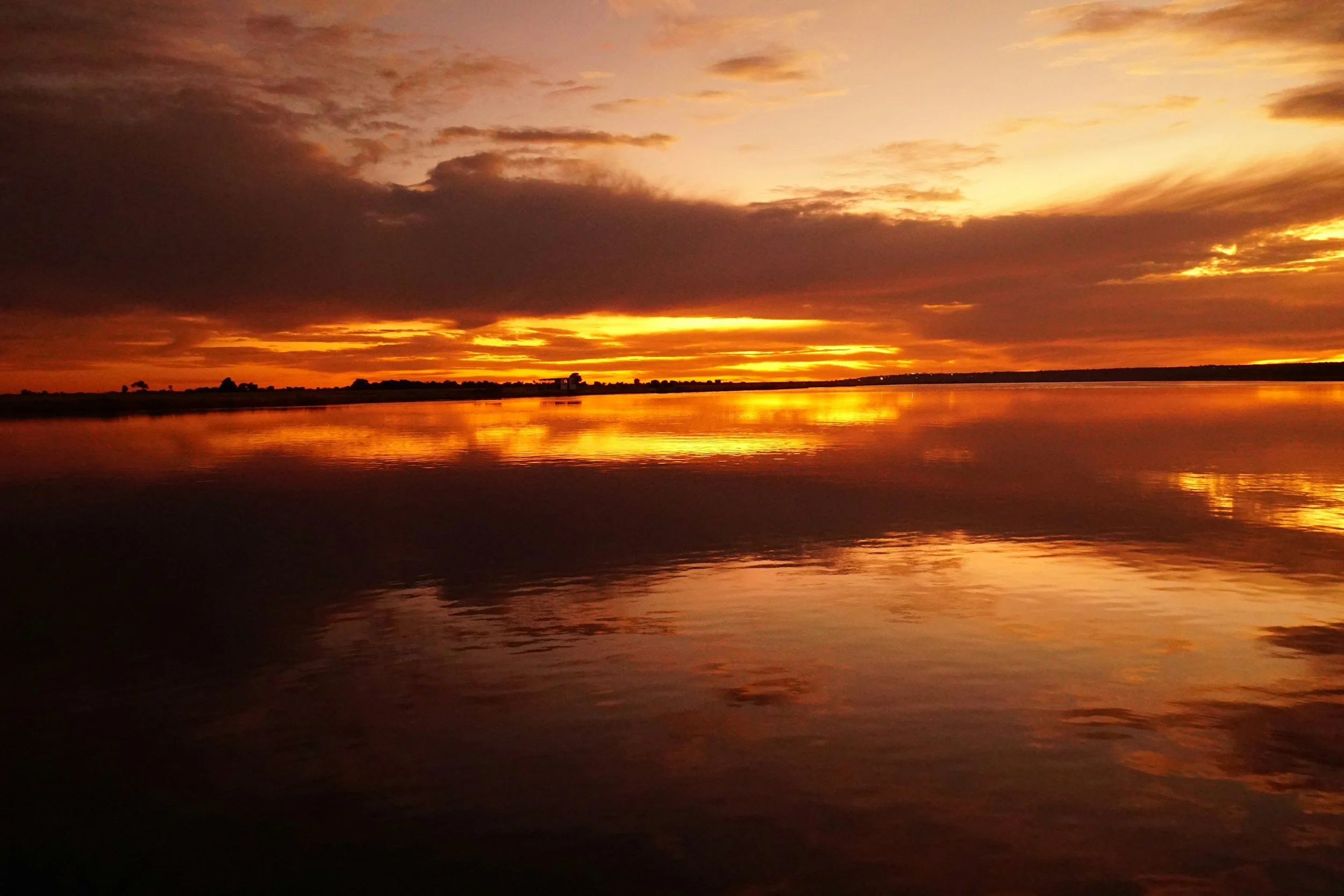 A sunset over a body of water with clouds in the sky, reflecting orange and yellow hues.