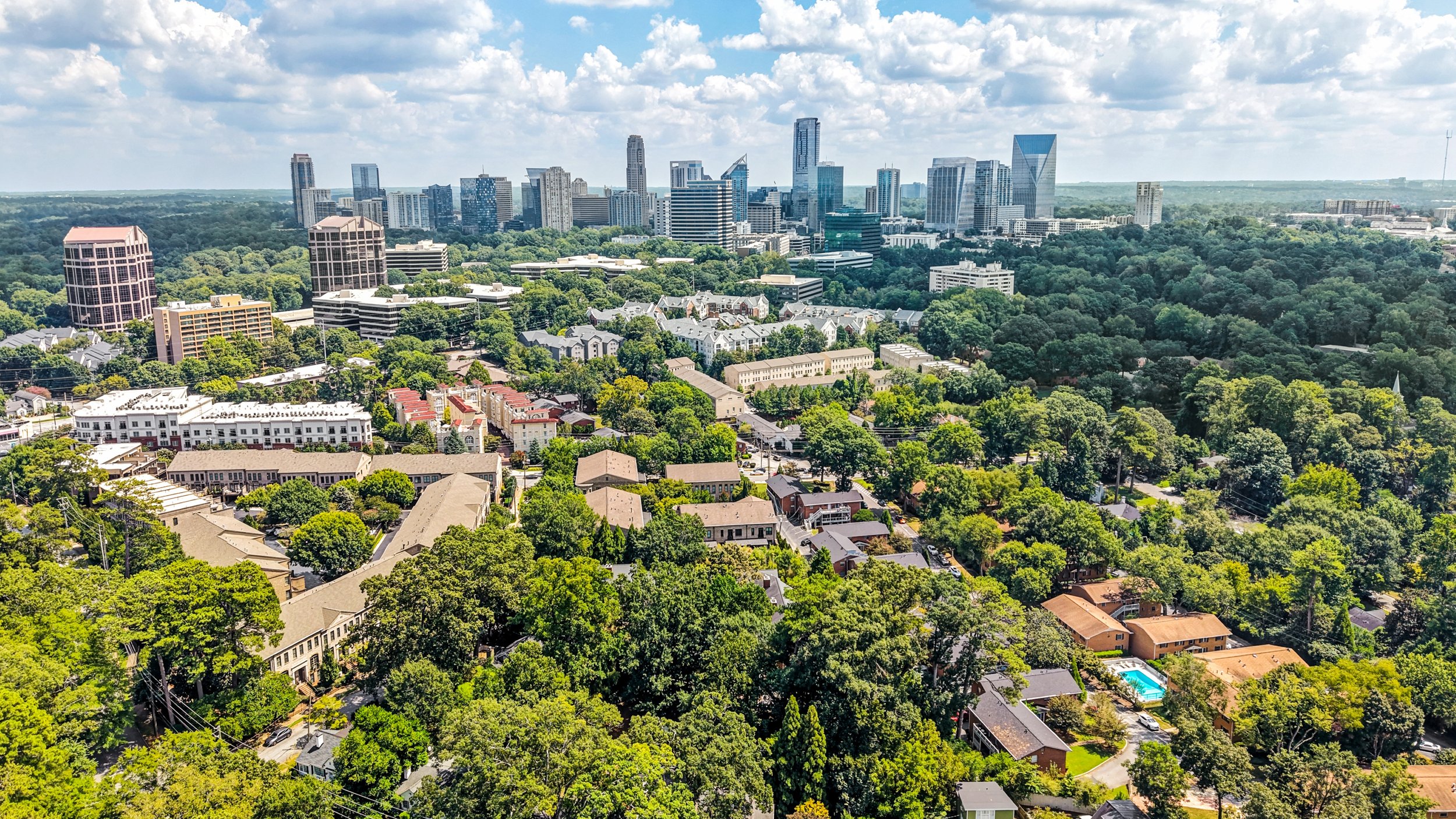 Aerial view of Buckehead Atlanta with tall skyscrapers in the background and residential houses with trees in the foreground.