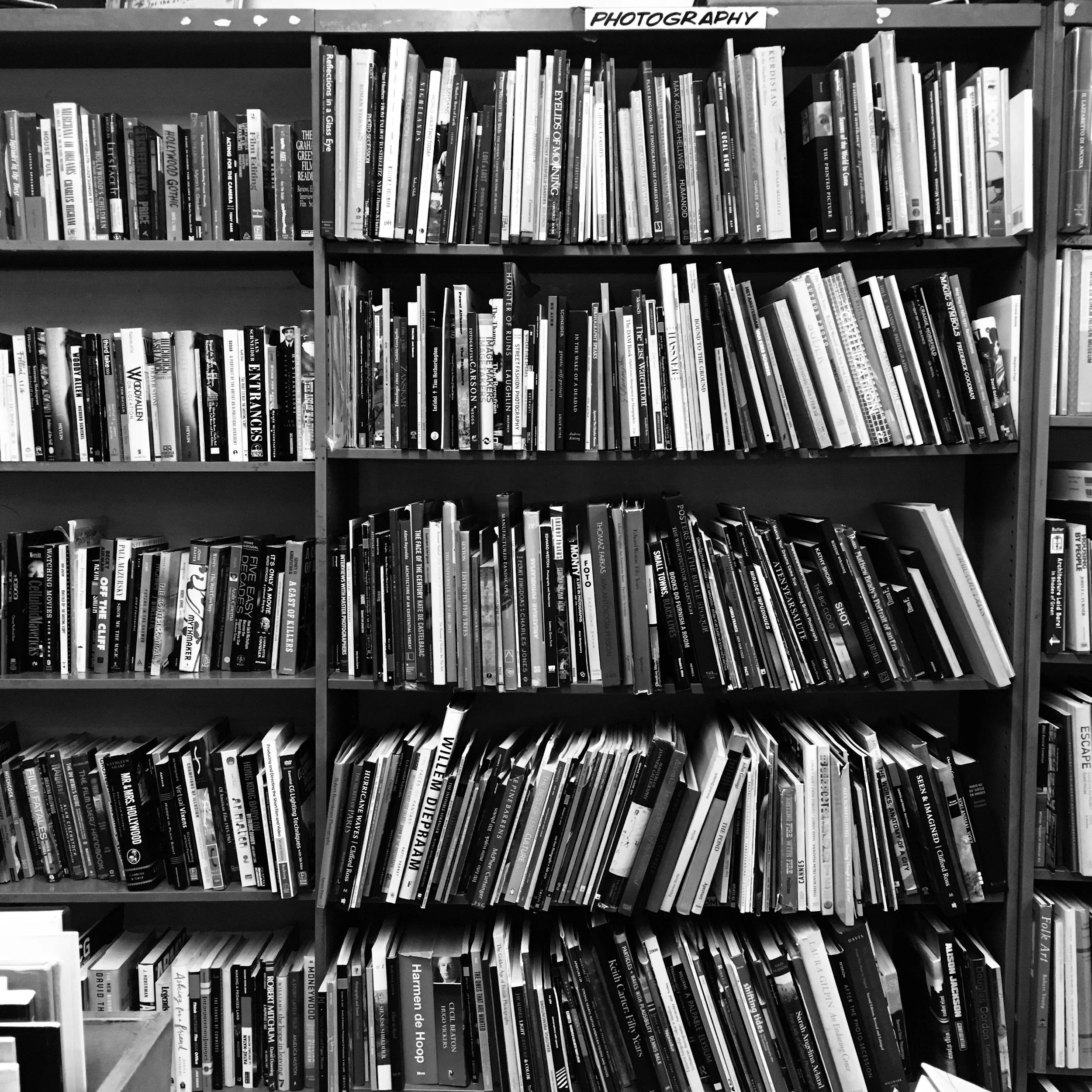 A bookshelf labeled 'PHOTOGRAPHY' at the top, filled with various books, some stacked horizontally, in black and white.