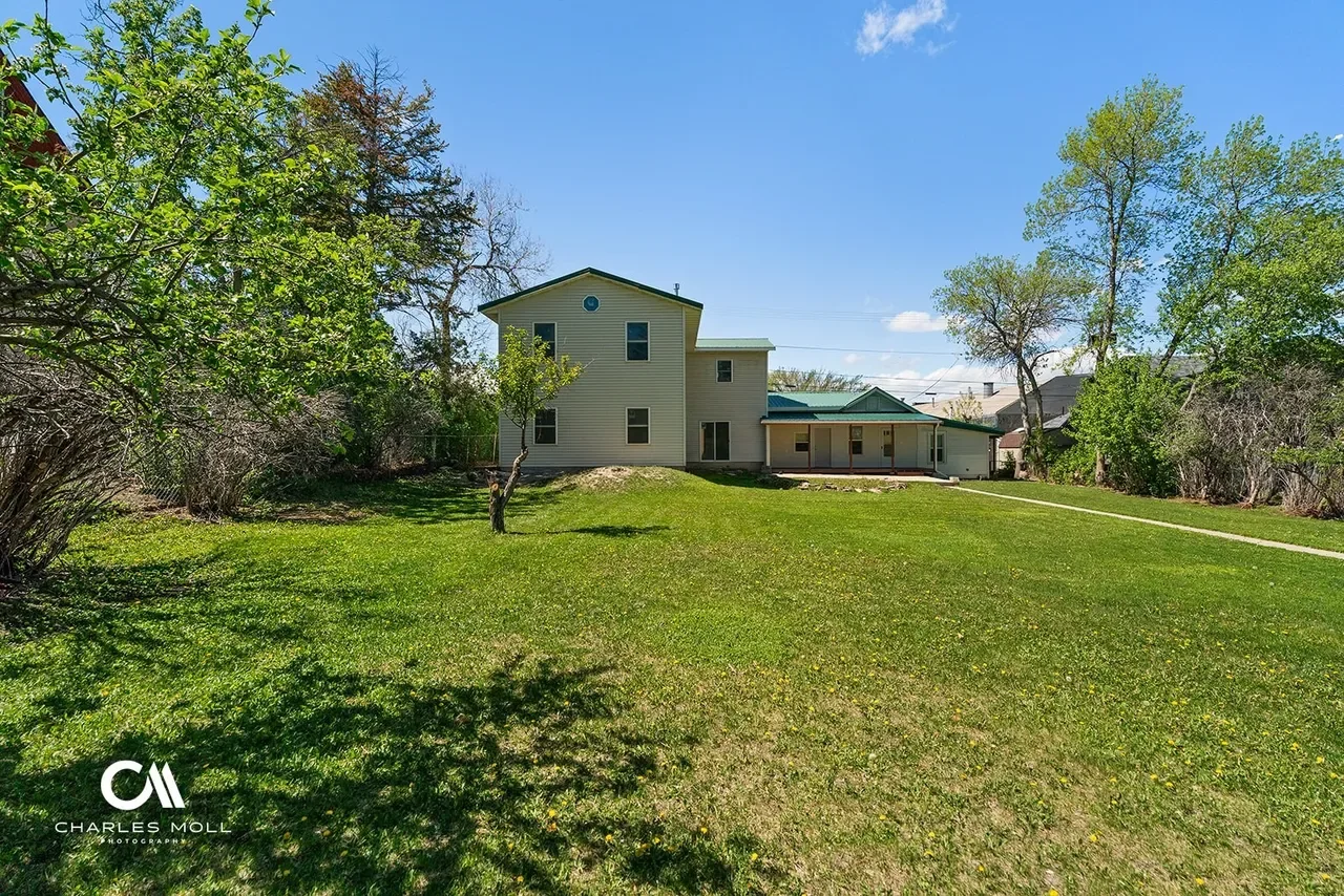Backyard of a house with green grass, trees, and a clear sky.