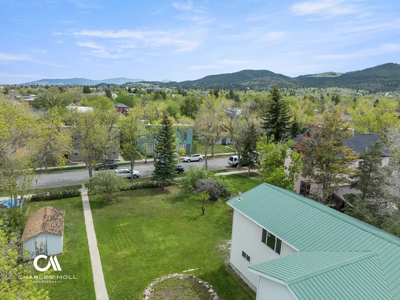 Aerial view of a suburban neighborhood with houses, trees, and streets, with mountains in the background under a partly cloudy sky.