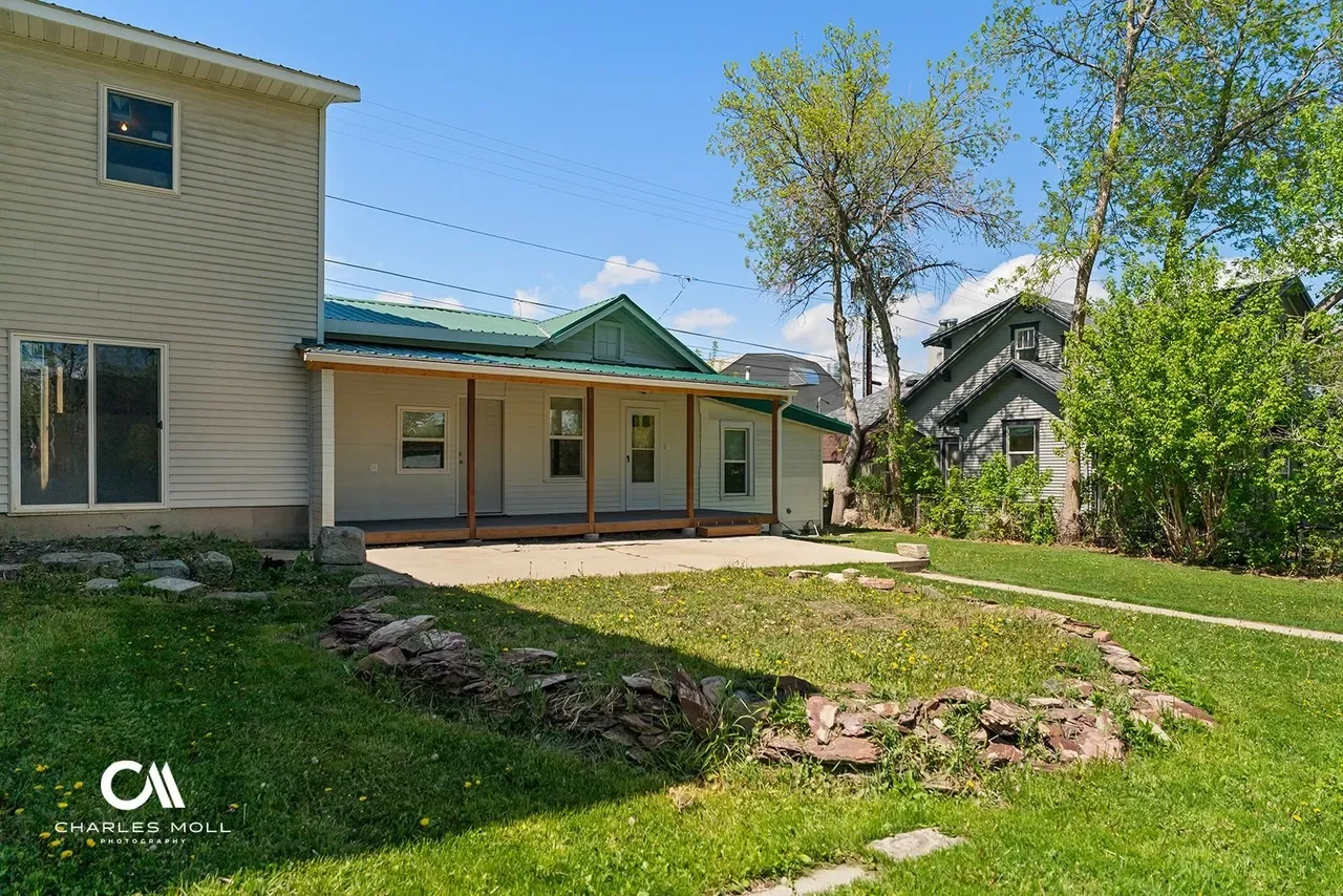 Backyard of a house with a newly built porch, green lawn, trees, and neighboring houses under a blue sky.