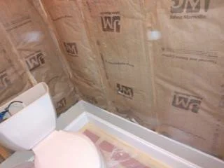 Bathroom corner with a white toilet and insulation on the wall.