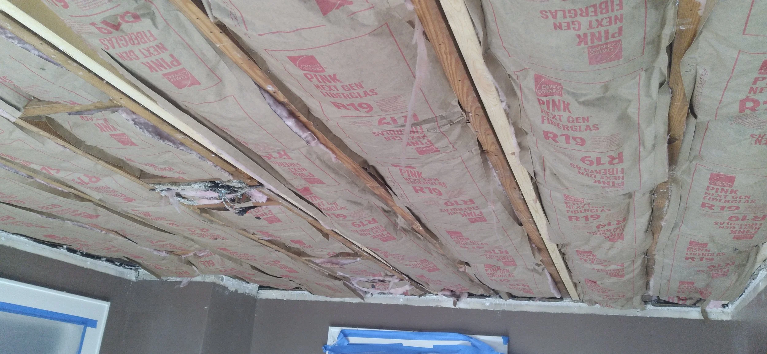 Ceiling under construction with pink fiberglass insulation installed between wooden rafters.