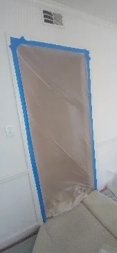 Door frame covered with plastic sheeting taped along the edges to protect the doorway.