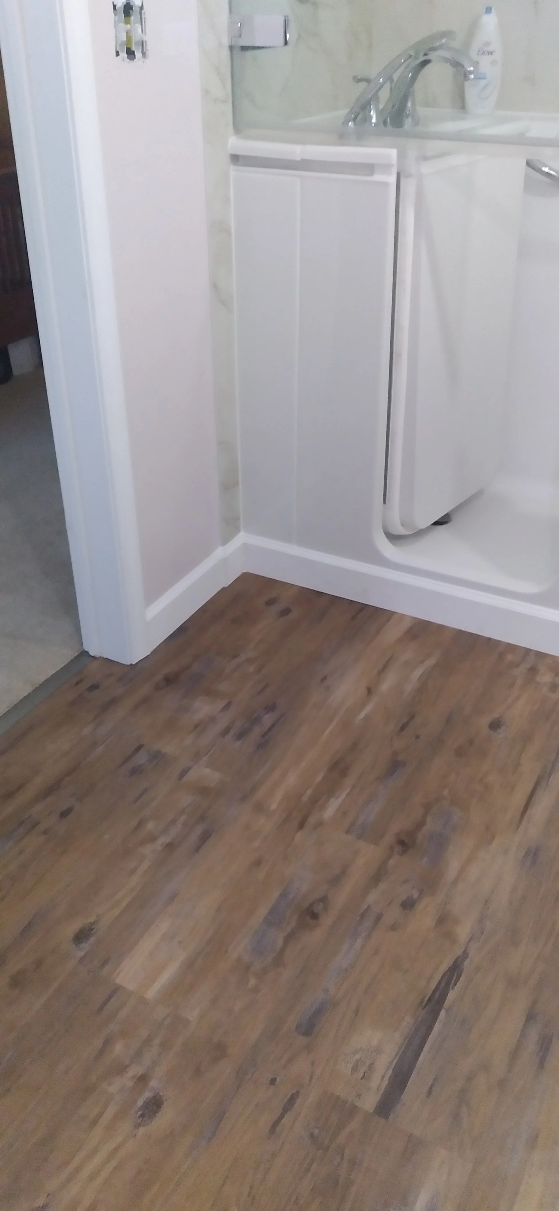 A corner of a bathroom showing a washing machine next to a small sink and mirror, with wood flooring and white trim.