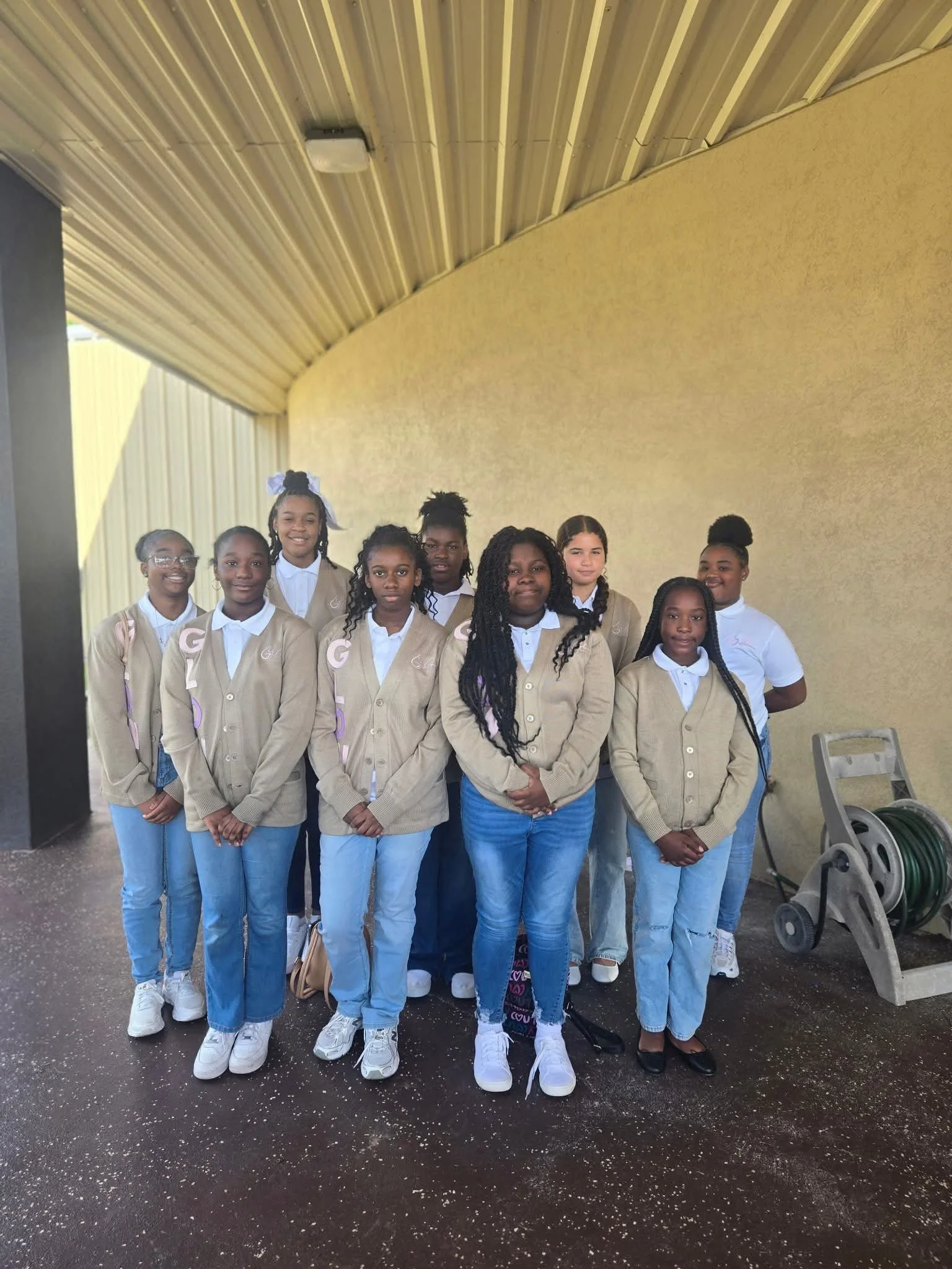 GLOW girls posing outdoors in matching cardigans, white shirts, and jeans.