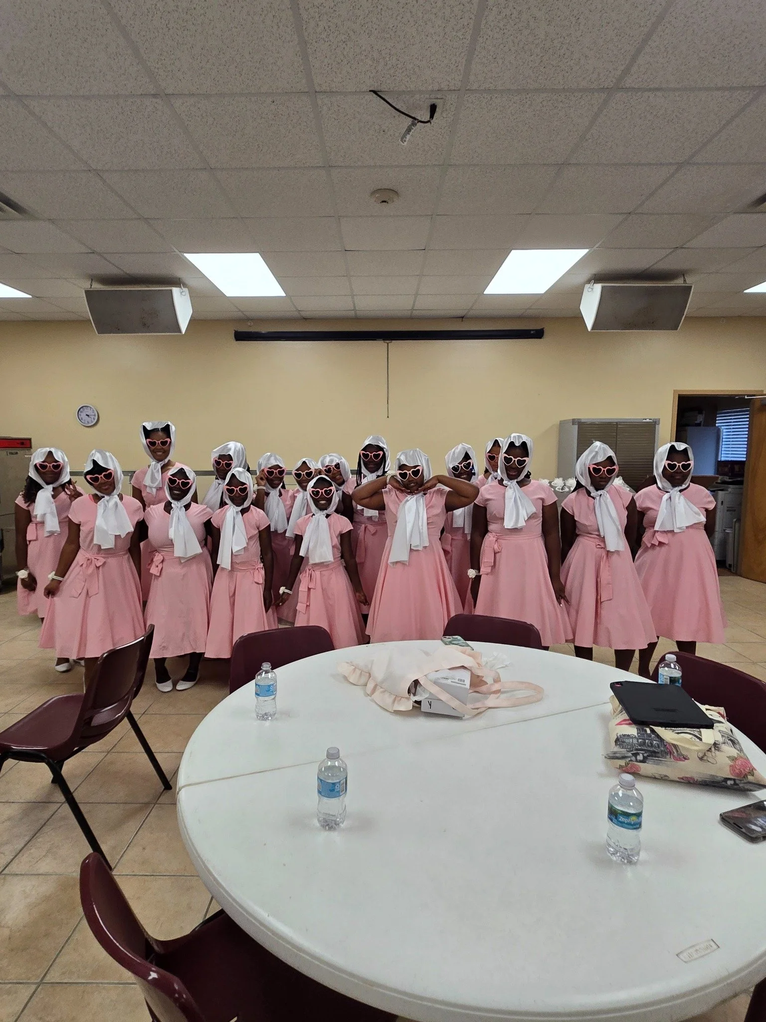GLOW girls wearing pink dresses, white scarves, and heart-shaped sunglasses before a performance.