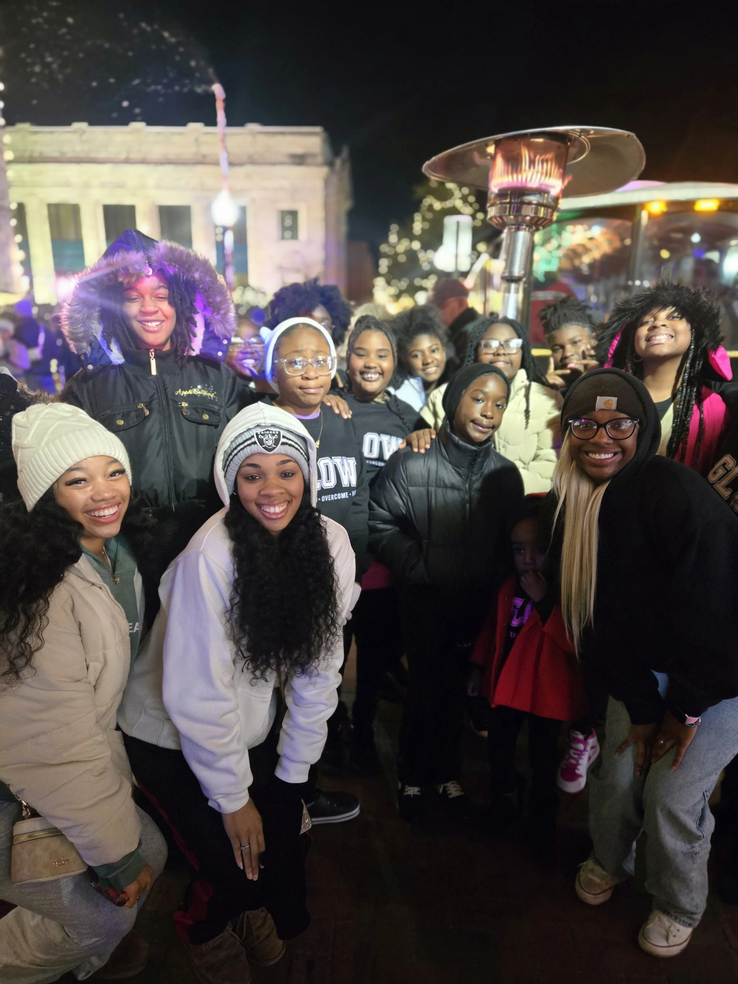 Group of people smiling and posing for a photo at an outdoor event at night, with colorful lights and a building in the background.