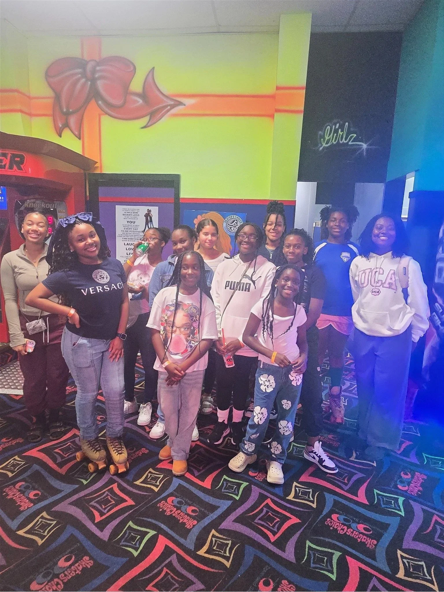 A group of children and teenagers posing together inside a colorful arcade or entertainment center, some smiling and wearing casual clothes, with a neon