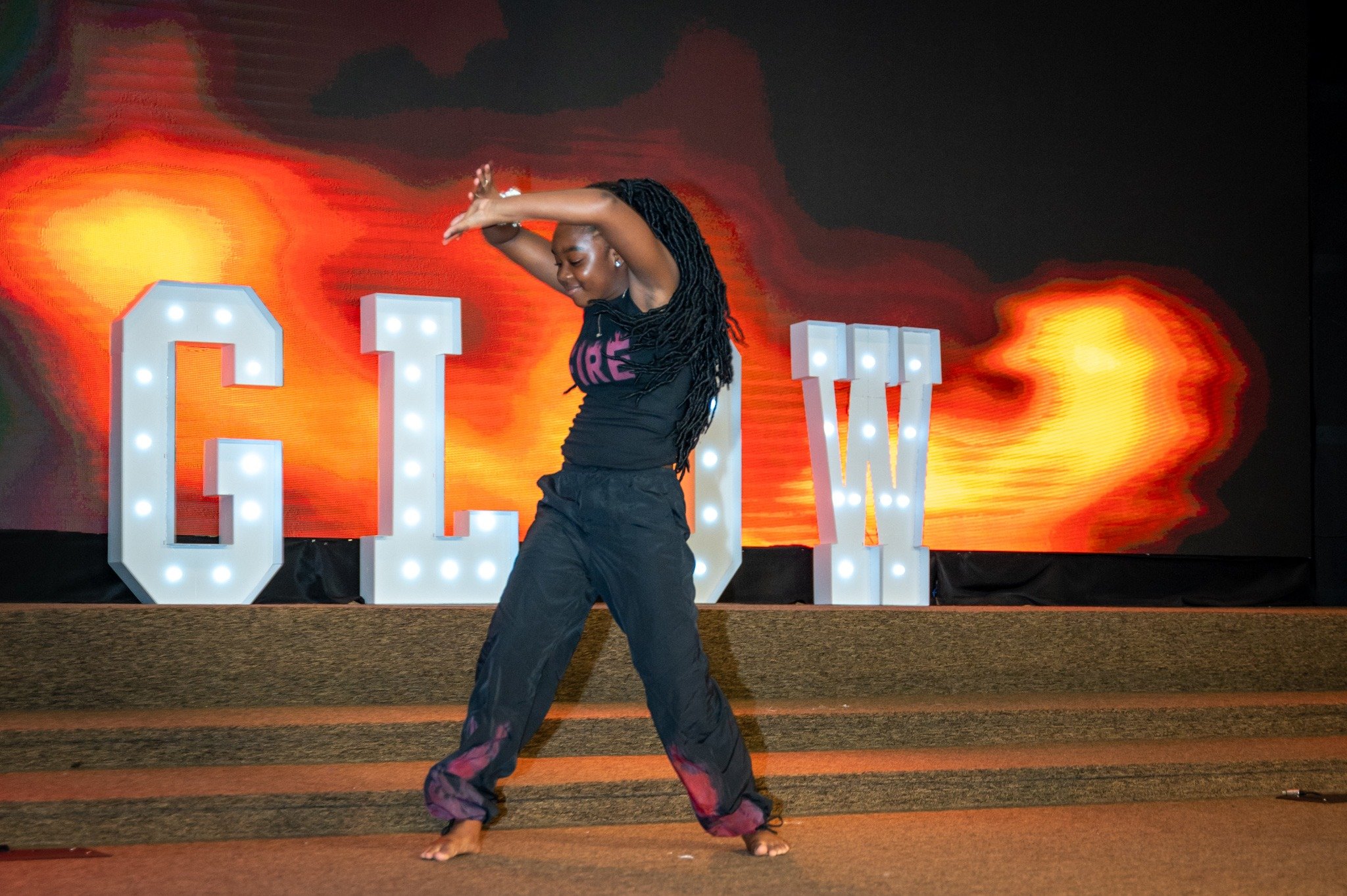 A GLOW dancer performs on stage in front of illuminated GLOW letters.