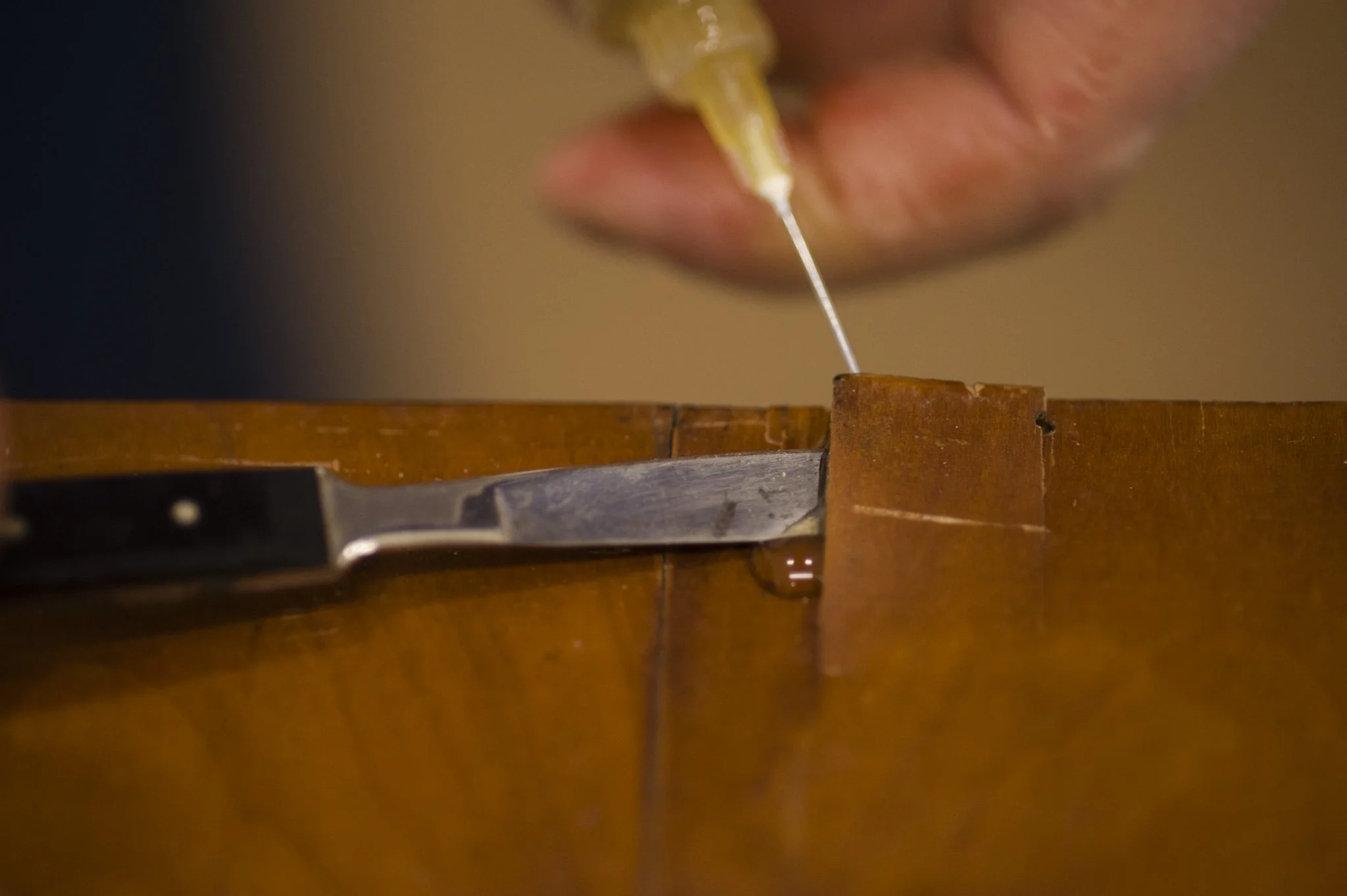 Nahaufnahme einer Hand, die ein Messer hält, und ein Holzstück, auf dem gearbeitet wird, während jemand eine Pipette benutzt.