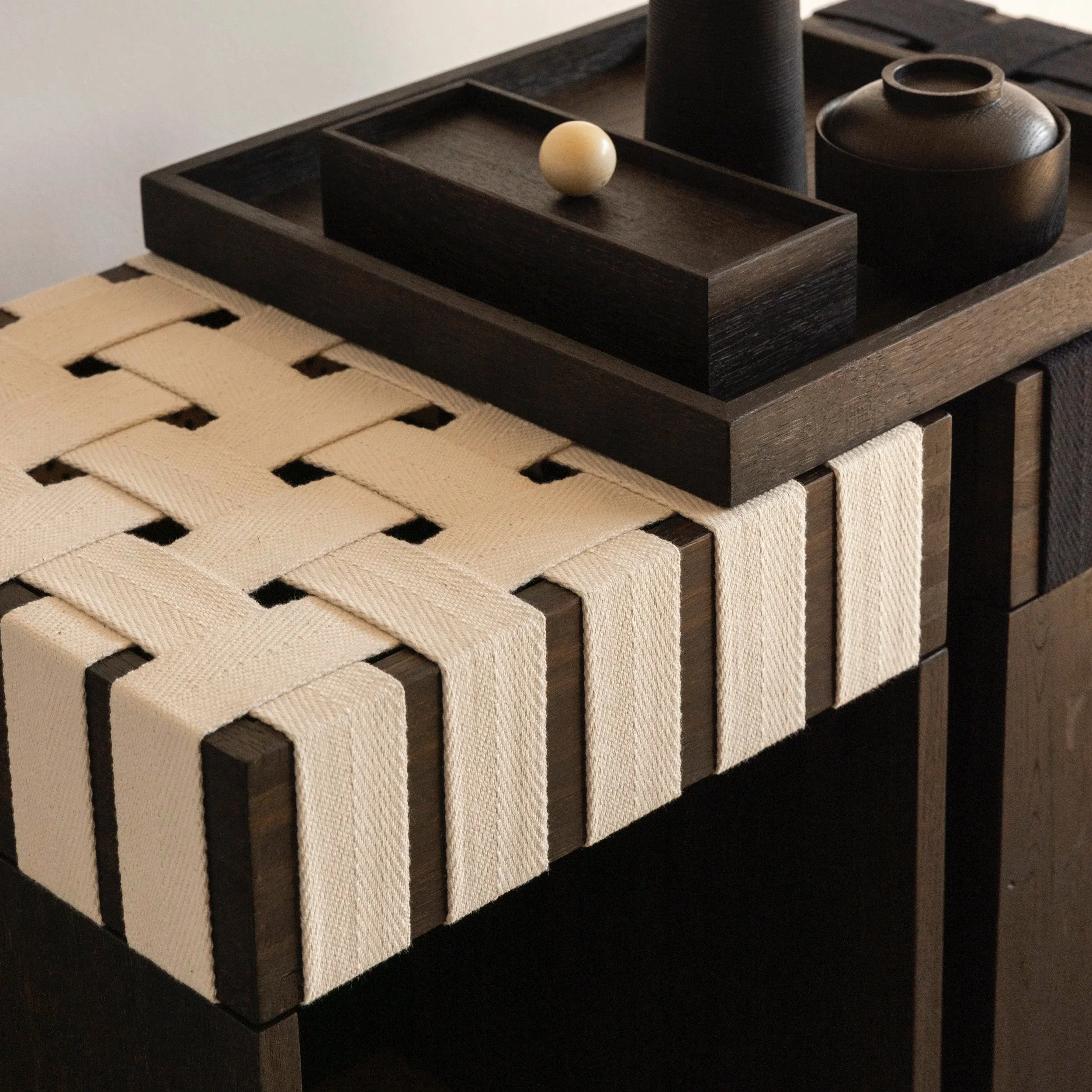 Dunkler Holztablett mit schwarzen Keramikvasen und einer kleinen hellen Holzfigur auf einem Holztisch.