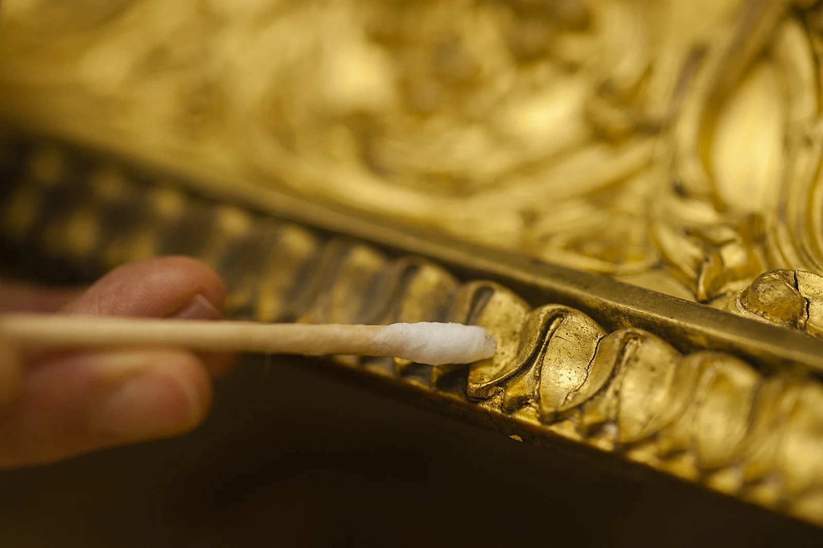 Hand putzt eine goldene Statue mit einem Wattestäbchen