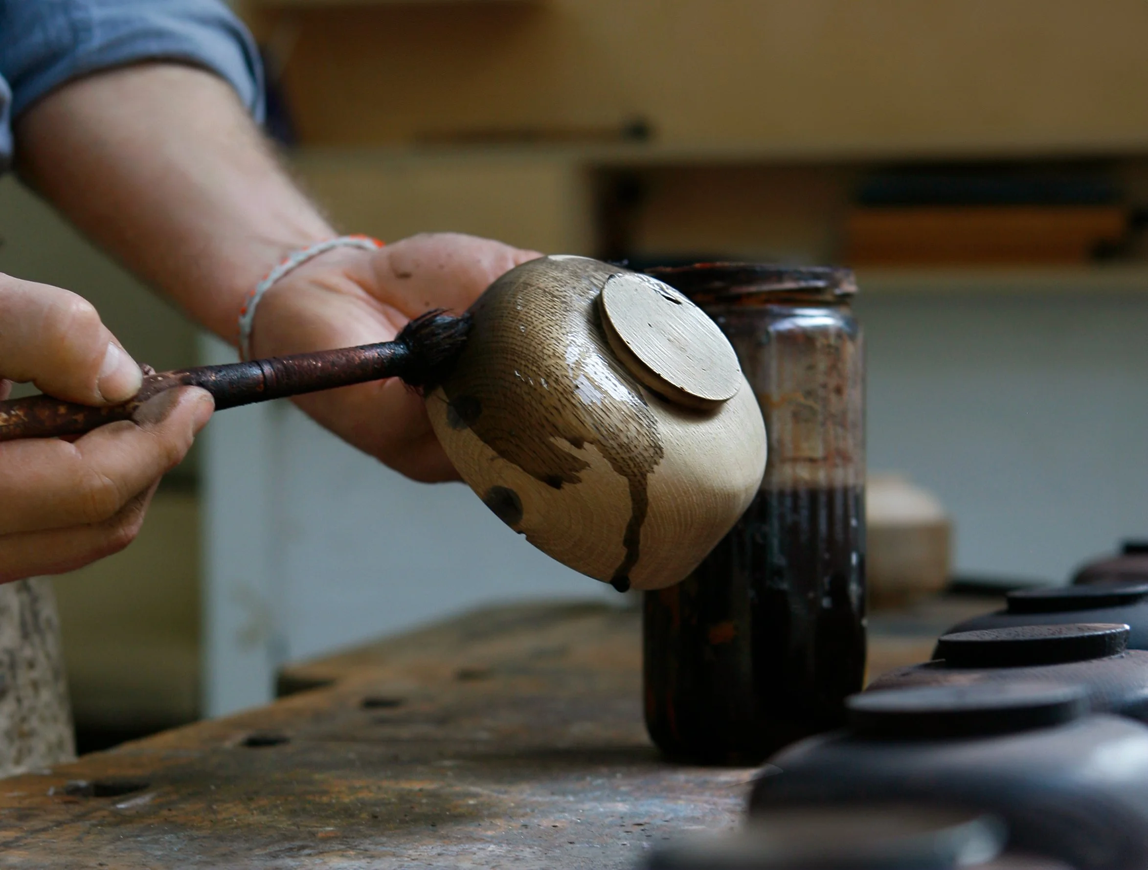 Hand, die eine Holzfigur mit einem Pinsel bemalt, in einer Werkstatt.