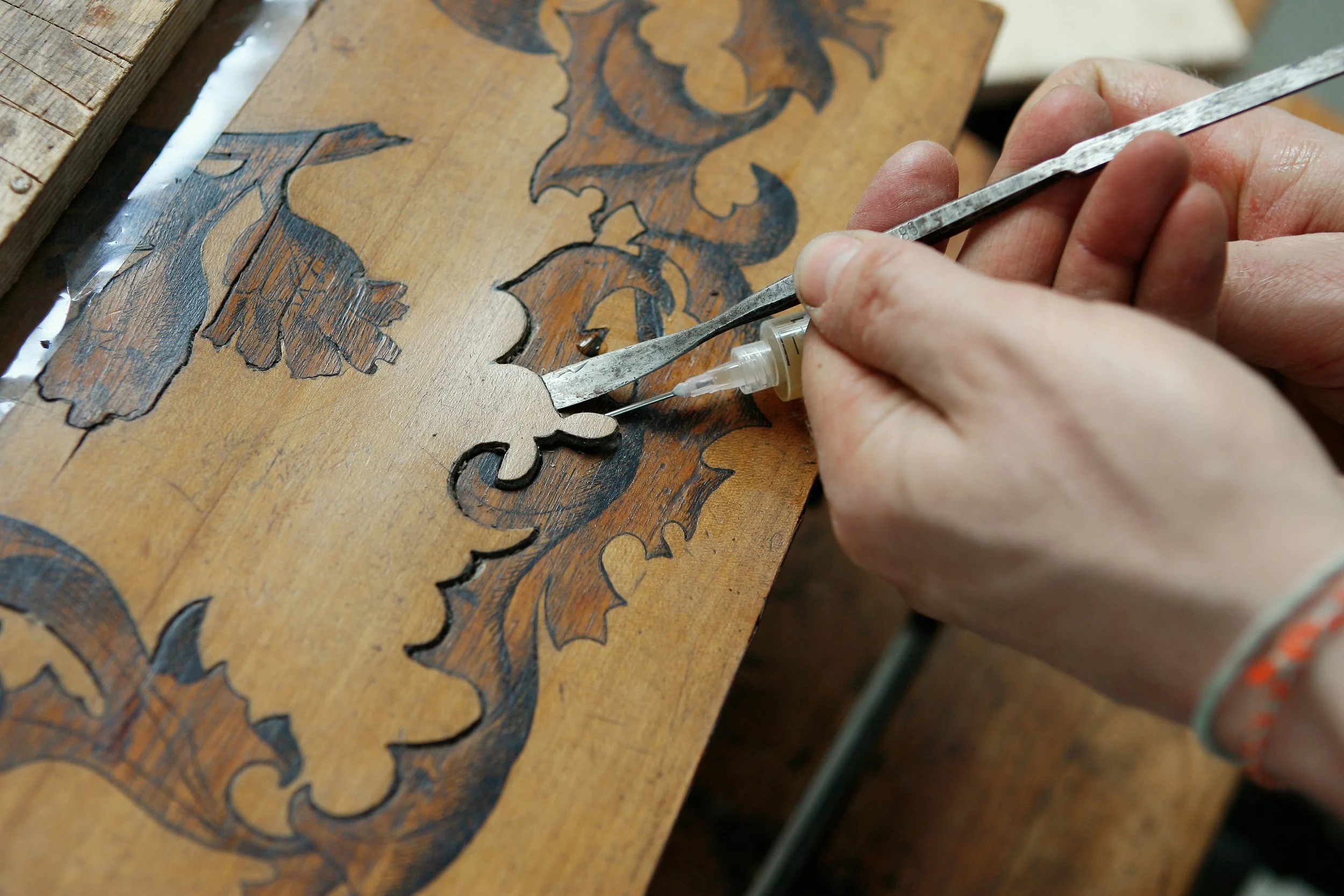 Hand eines Künstlers arbeitet an einer Holztisch mit detailliertem Schnitzmuster, Werkzeuge in der Hand, um das Design aus Holz zu schneiden.