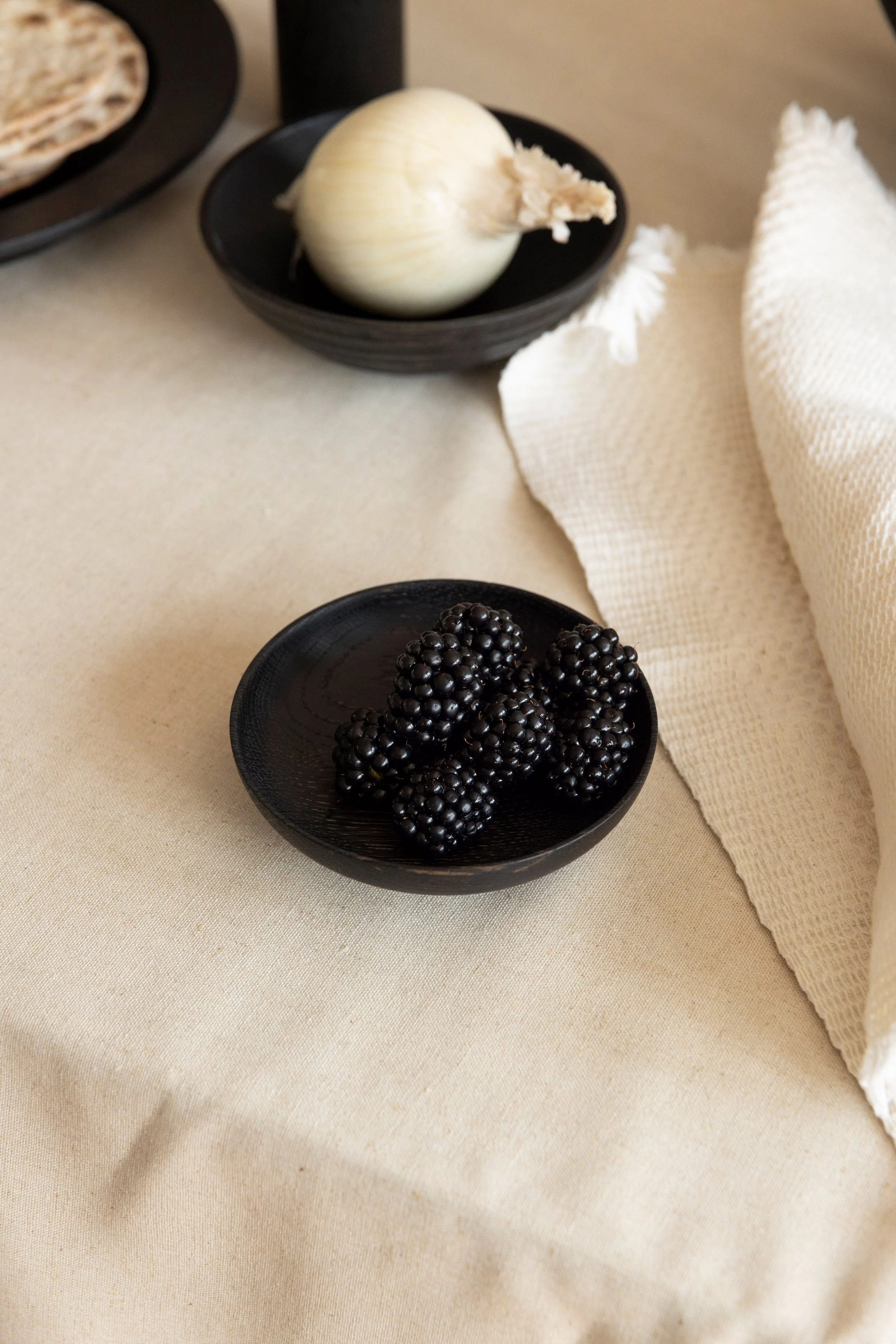 Schwarze Beeren in einer schwarzen Schüssel auf einem hellen Tuch