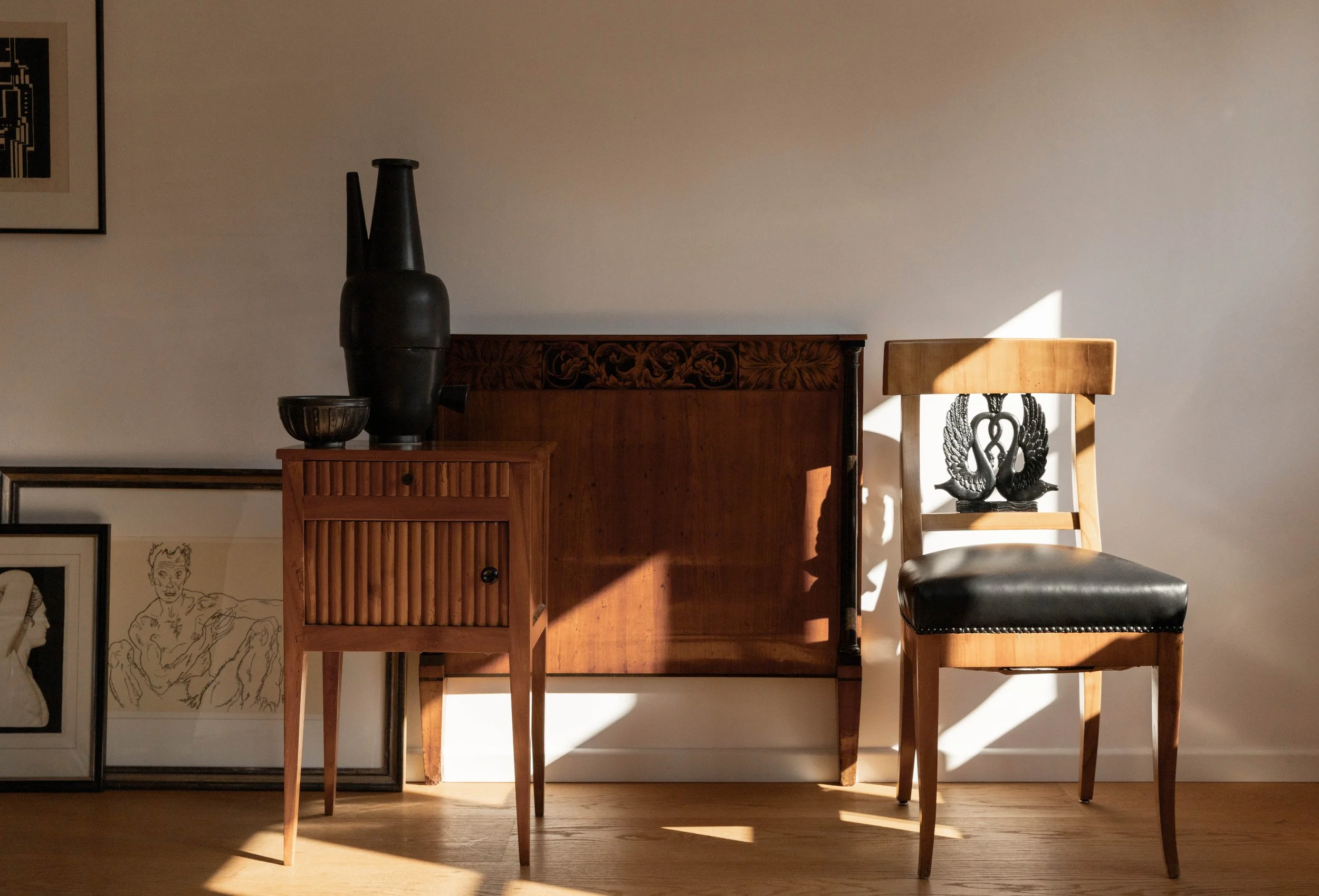 Ein Innenraum mit Holzmöbeln und Kunstwerken, Sonnenstrahlen fallen durch ein Fenster und beleuchten den Raum.