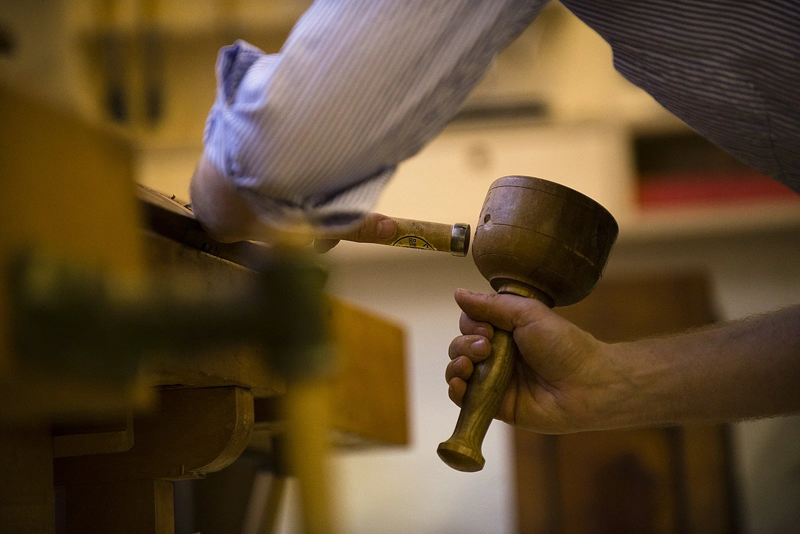 Person schlägt einen hölzernen Kochlöffel auf einen Holzhammer, in einer Werkstatt oder Küche