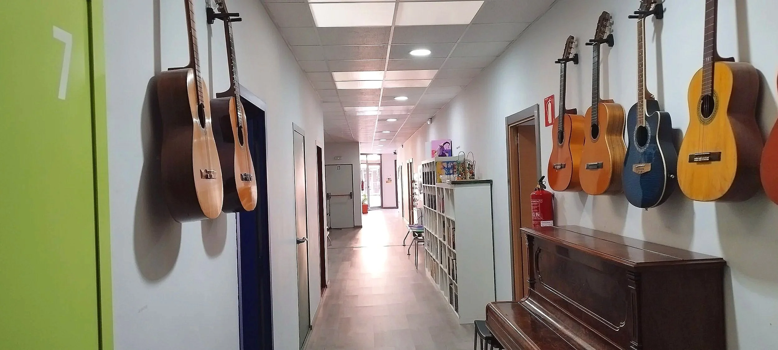 Pasillo con guitarras colgadas en la pared, a la izquierda una puerta verde y a la derecha mobiliario y objetos decorativos.