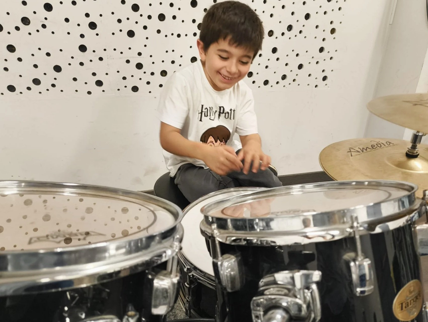 Infant somrient tocant la bateria en una sala de música.