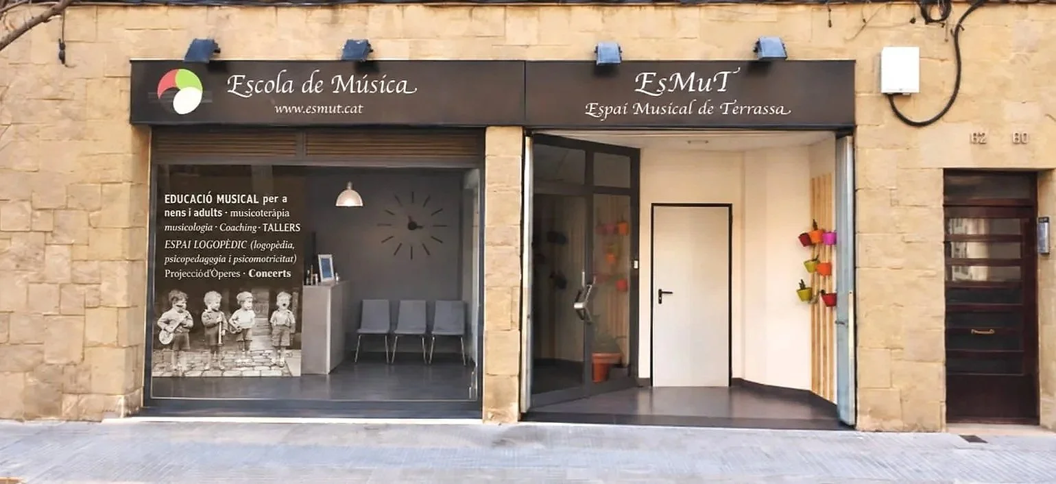fachada de una escuela de música llamada EsMuT, Espai Musical de Terrassa, con cartel que describe servicios musicales, y un interior visible con sillas y decoración.