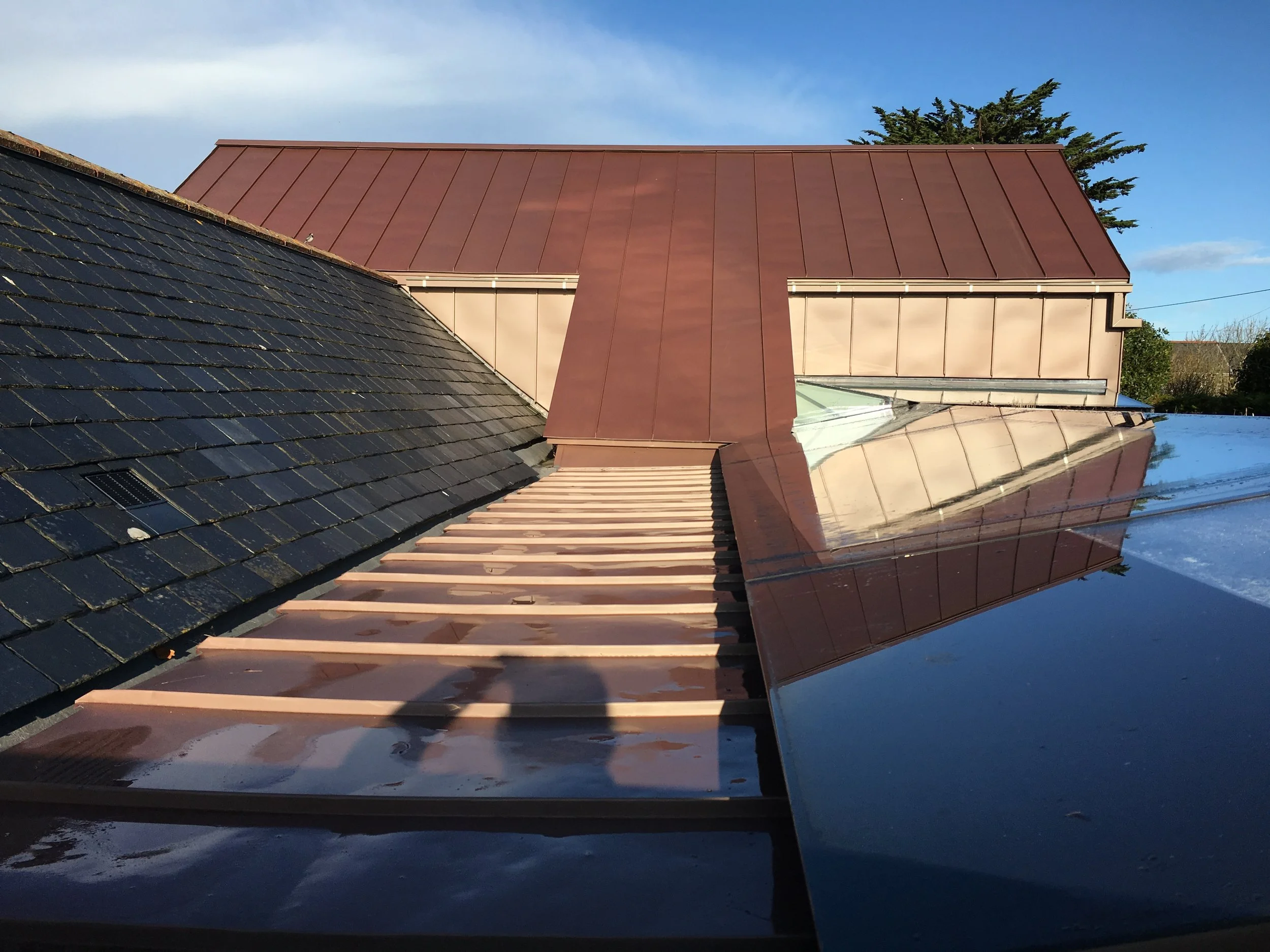 This project brings together existing slate roofs with a new standing-seam metal roof, using the change in material to clearly distinguish old from new. Carefully formed junctions, rooflights and concealed drainage resolve a complex roofscape while b