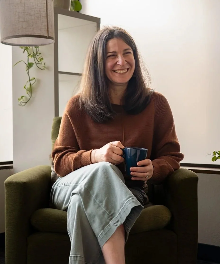 Smiling woman in a brown sweater sitting in an armchair and holding a blue mug