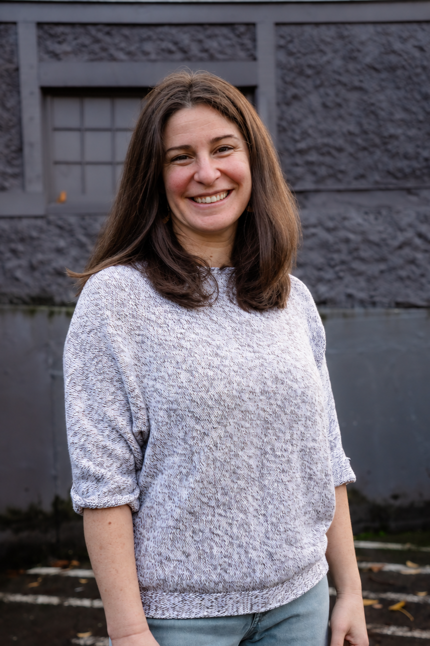 Smiling woman with long brown hair standing outdoors in front of a dark stone building