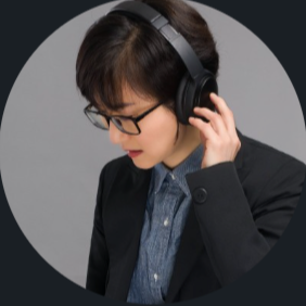 Young woman with short dark hair and glasses wearing headphones, looking down thoughtfully.