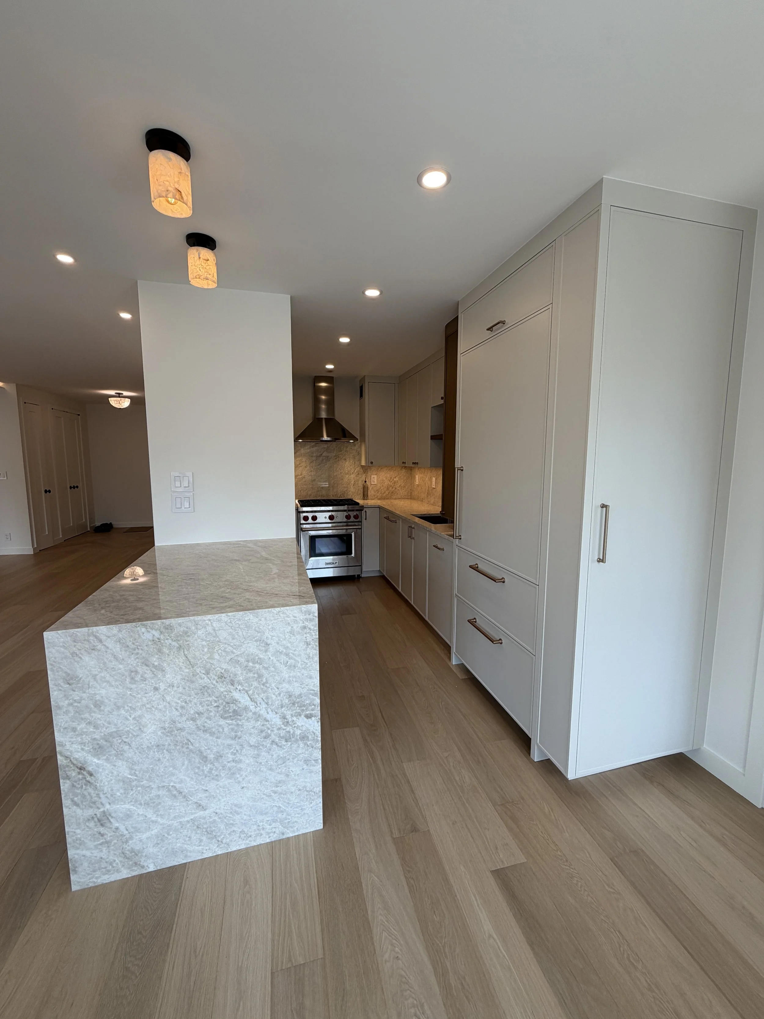 Modern kitchen with white cabinets, stainless steel stove, marble island, and hardwood flooring, with ceiling lights.
