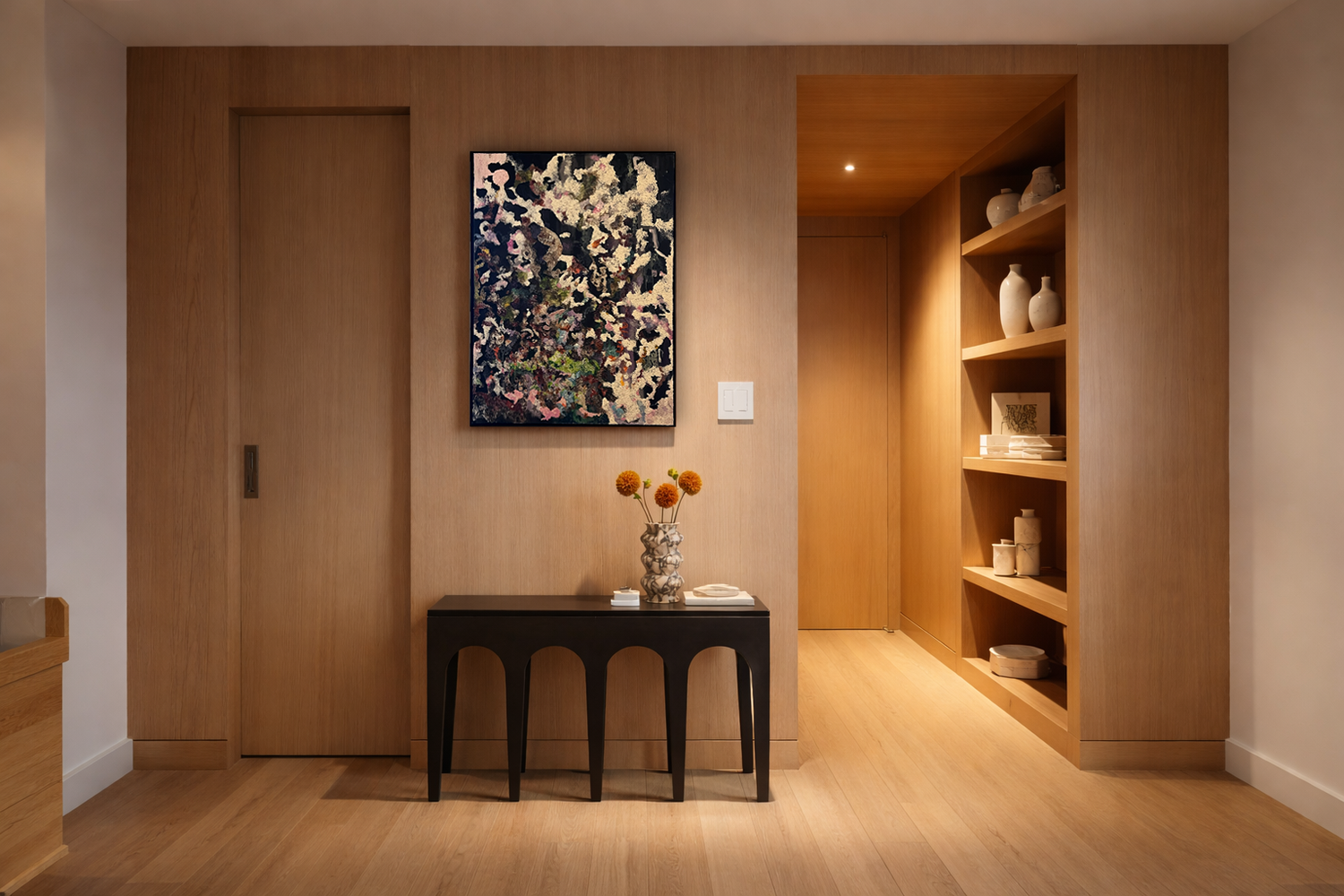 Modern room with wooden walls, black side table with flowers, abstract painting, built-in bookshelf with vases and decor.