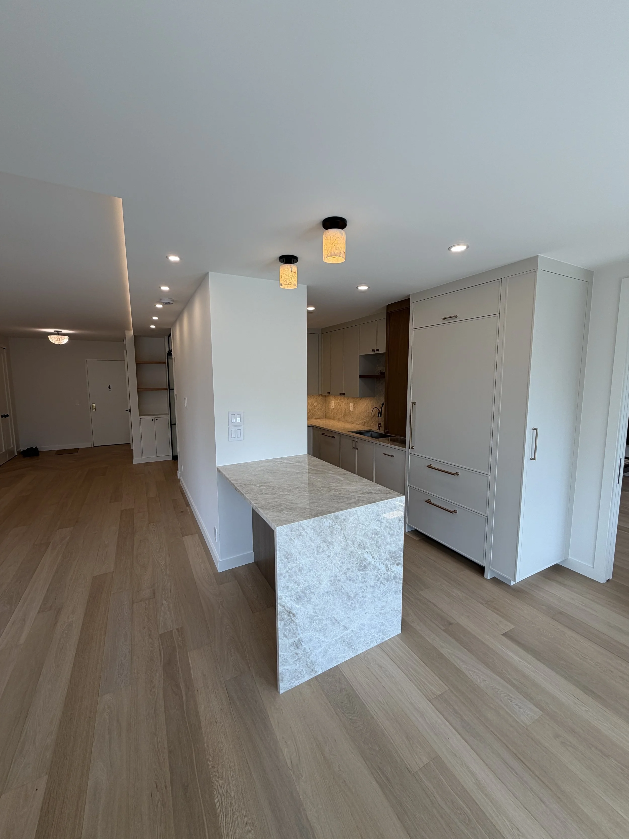 Interior of a modern kitchen with white and wood cabinets, a marble island, wood flooring, and ceiling lights.