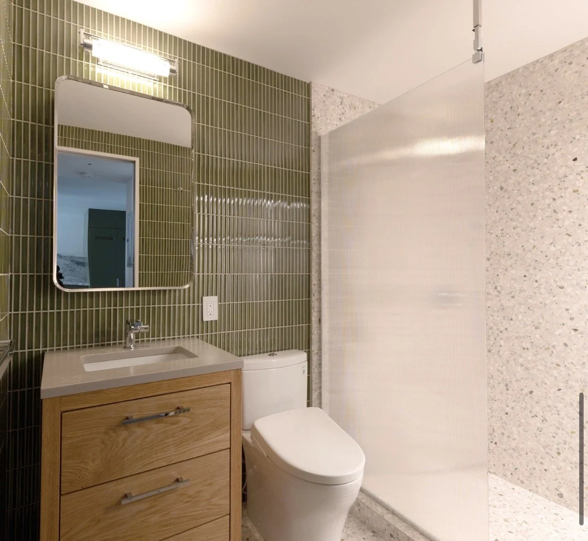 Modern bathroom with a wooden vanity, green tiled wall, mirror, toilet, and a plastic shower curtain.