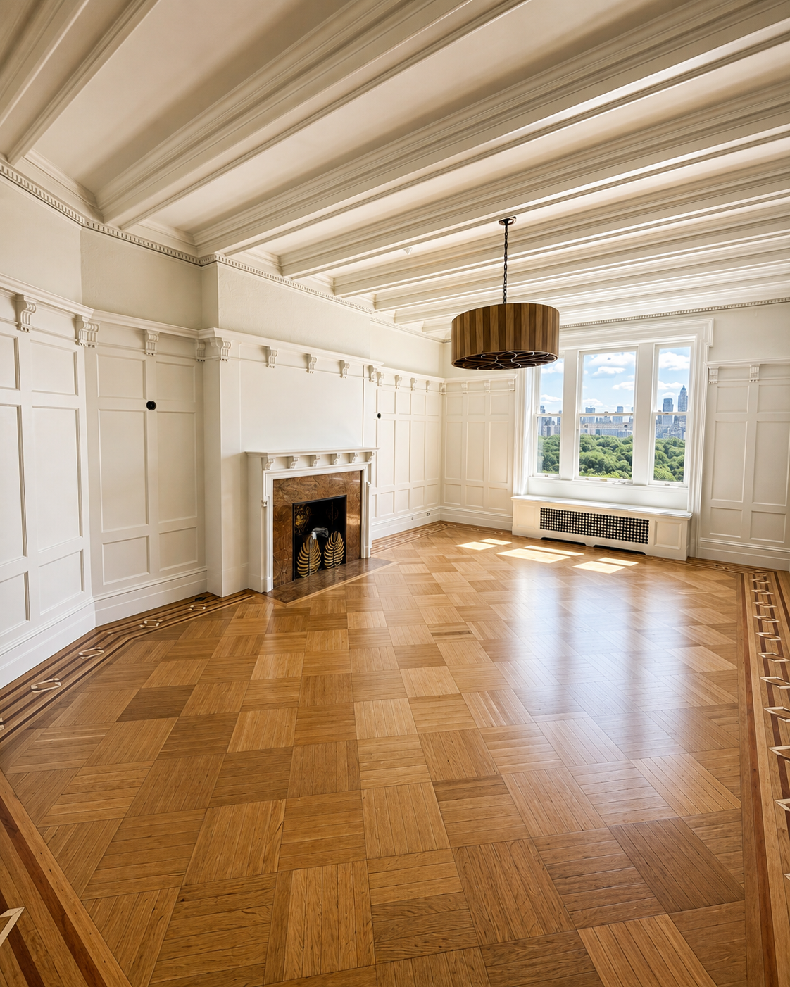 An empty room with white paneled walls, a large window showing a city skyline and green trees, a fireplace with a decorative mantel, and a wooden floor with intricate parquet pattern. A modern circular wooden chandelier hangs from the ceiling.