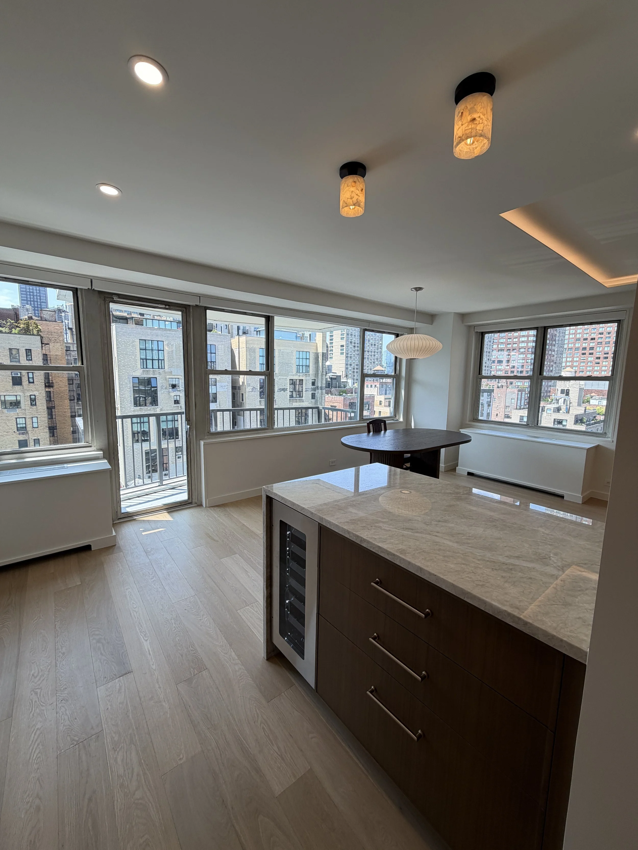 Modern apartment interior with large windows, a marble-topped kitchen island, and city skyline view.