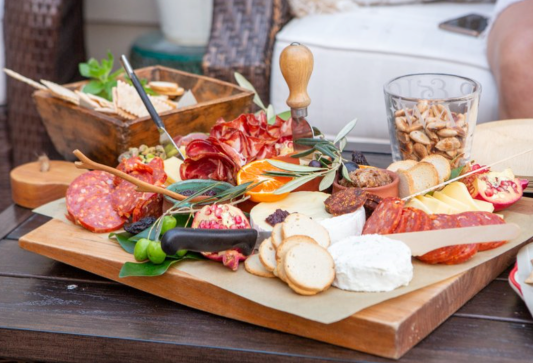 Charcuterie board with cheeses, meats, crackers, olives, and nuts on a wooden table.