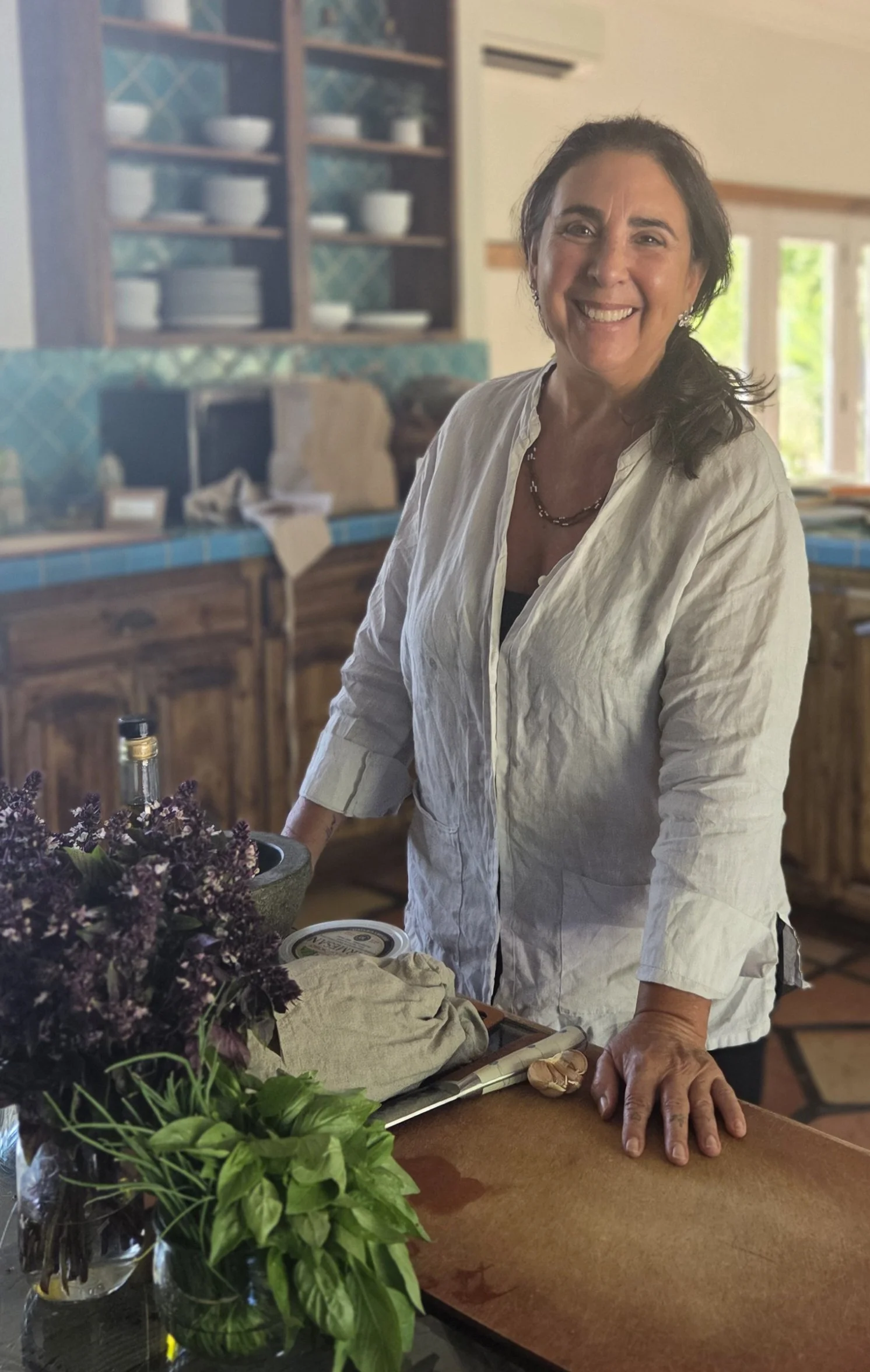 Chef Robin standing in a kitchen with herbs on the table ready to prep.