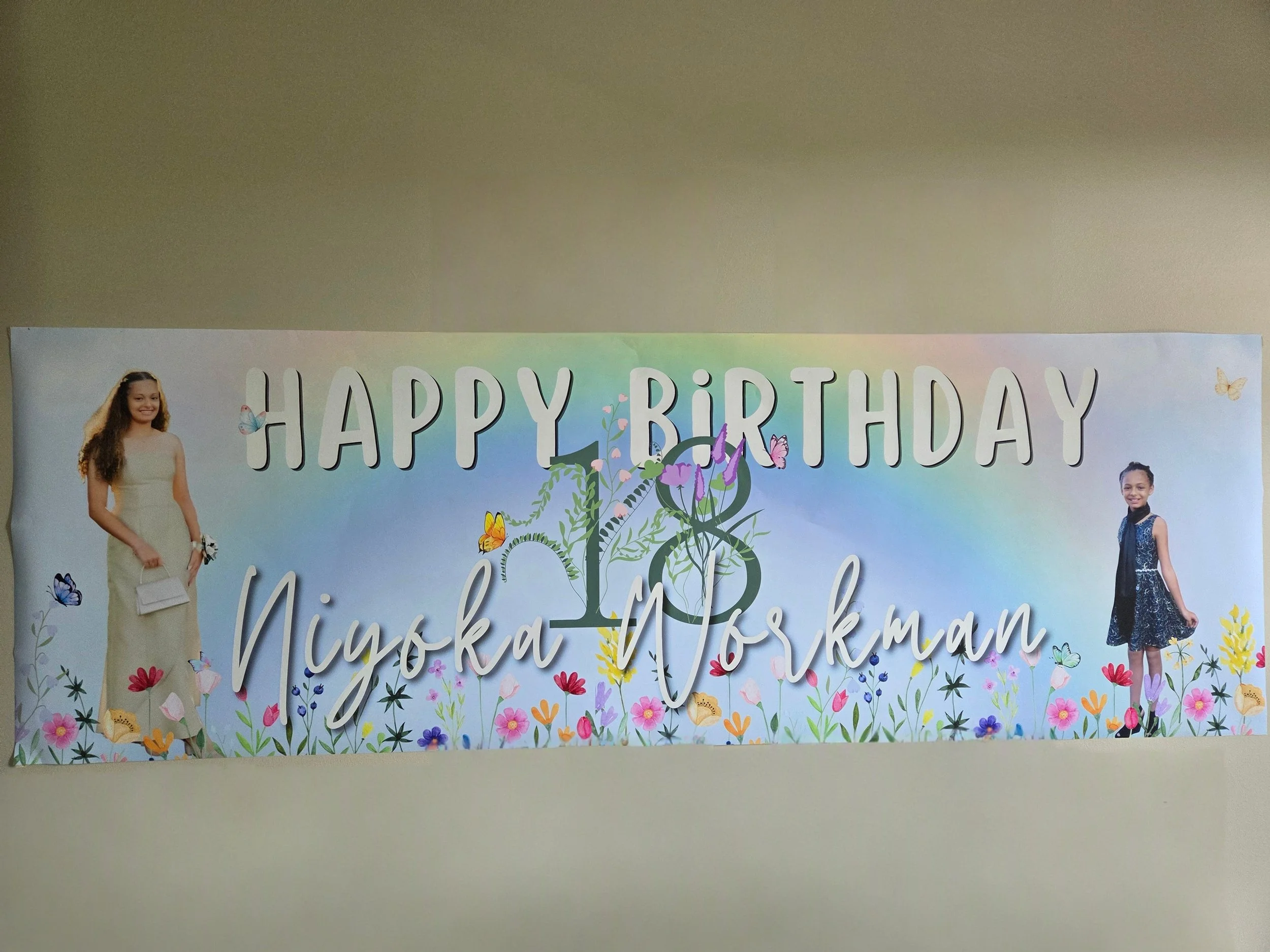 Decorative birthday banner with young girls on either side, surrounded by colorful flowers and butterflies, with the words "HAPPY BIRTHDAY" prominently displayed.