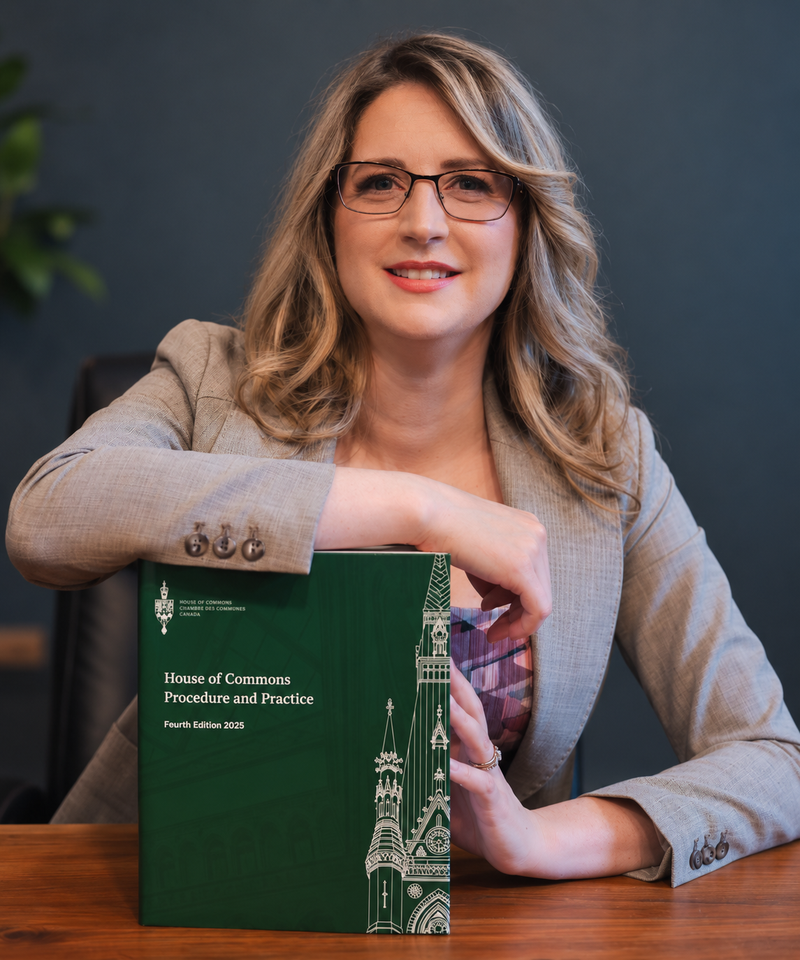 Tanya Davies, host of Unveiling Canada, seated with a House of Commons Procedure and Practice book.