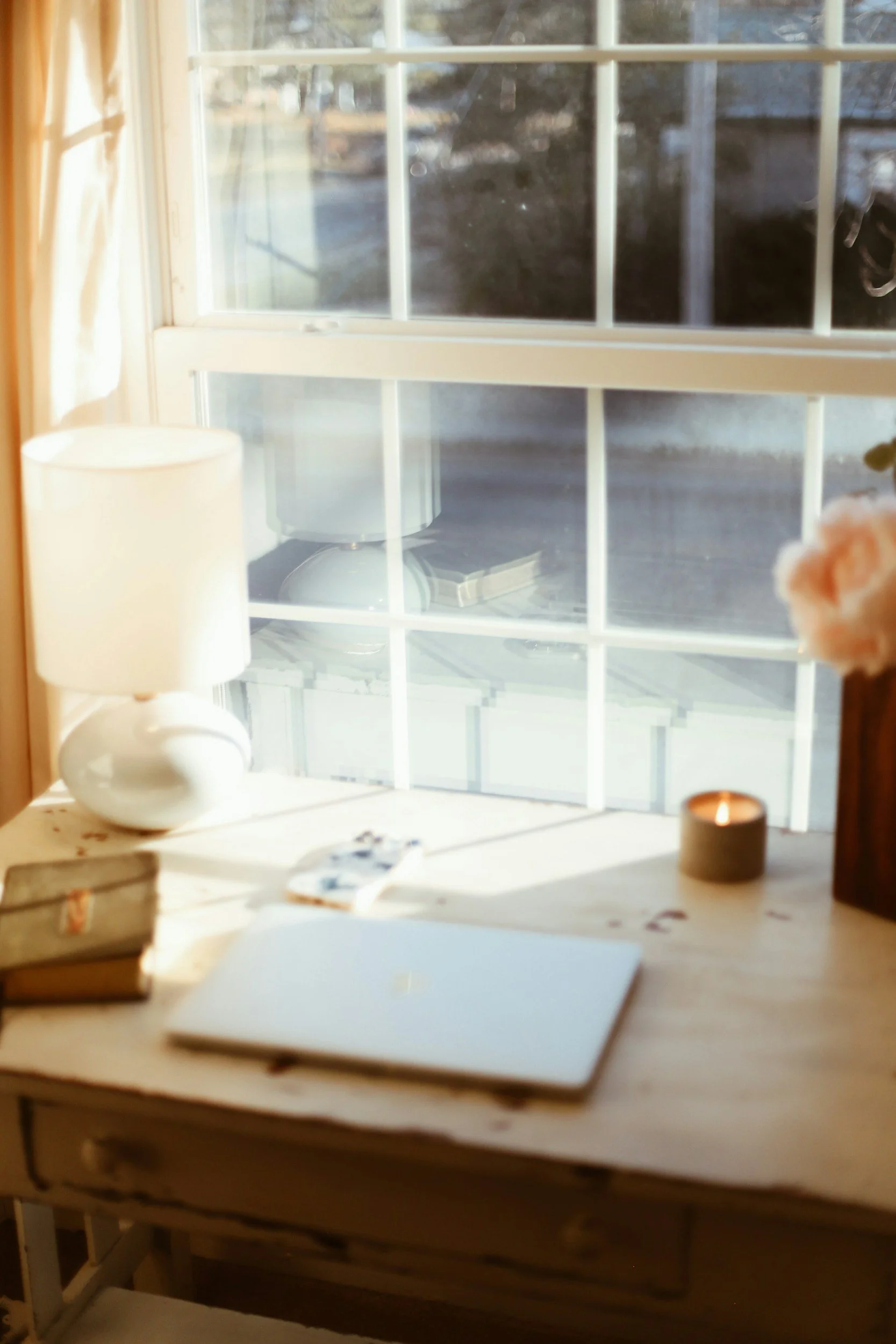 Desk with a laptop, lamp and candle by a sunlit window