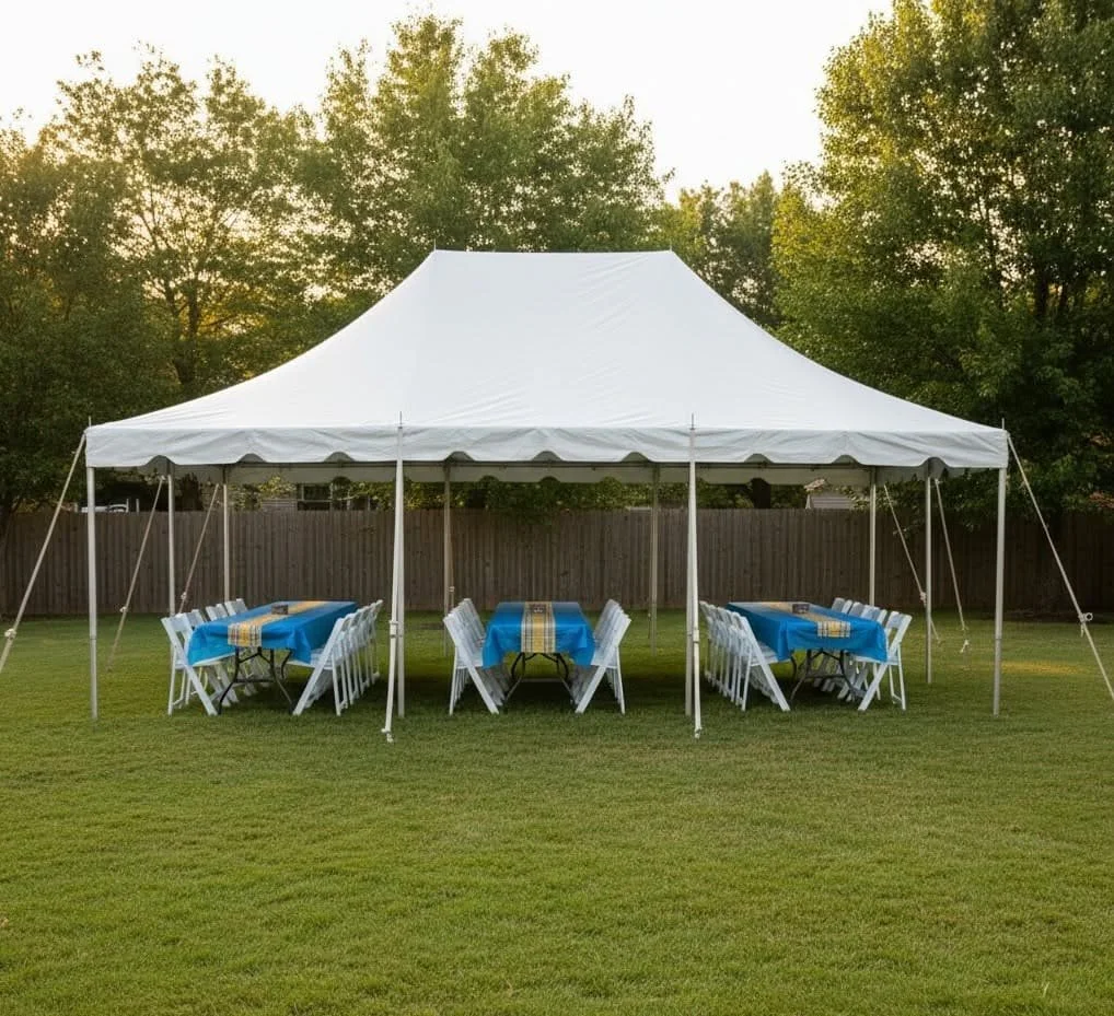 A white outdoor event tent with tables covered in blue tablecloths and white chairs on a grassy lawn surrounded by trees.