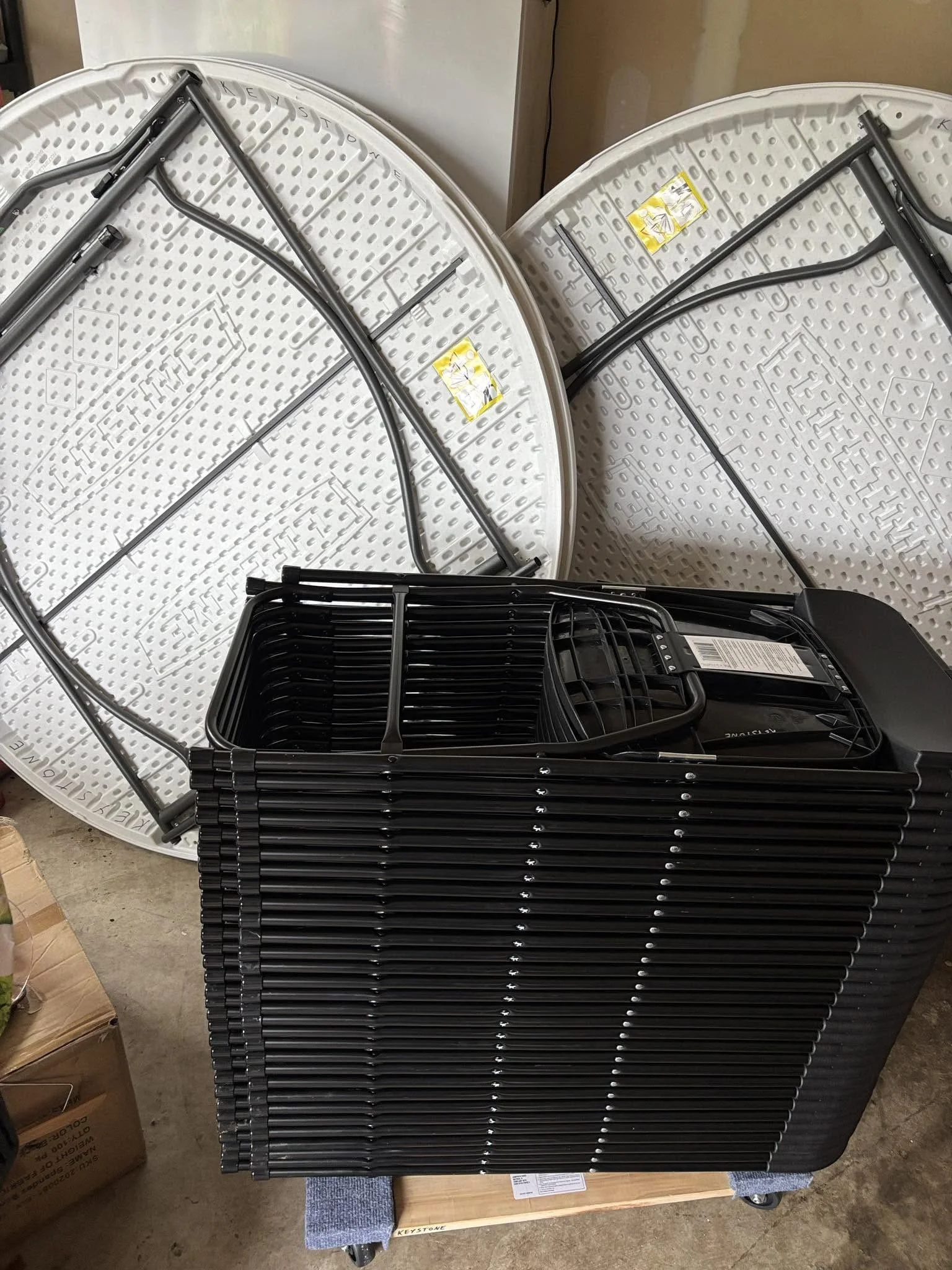 Two folded white patio tables with black metal legs, stacked on a cart.