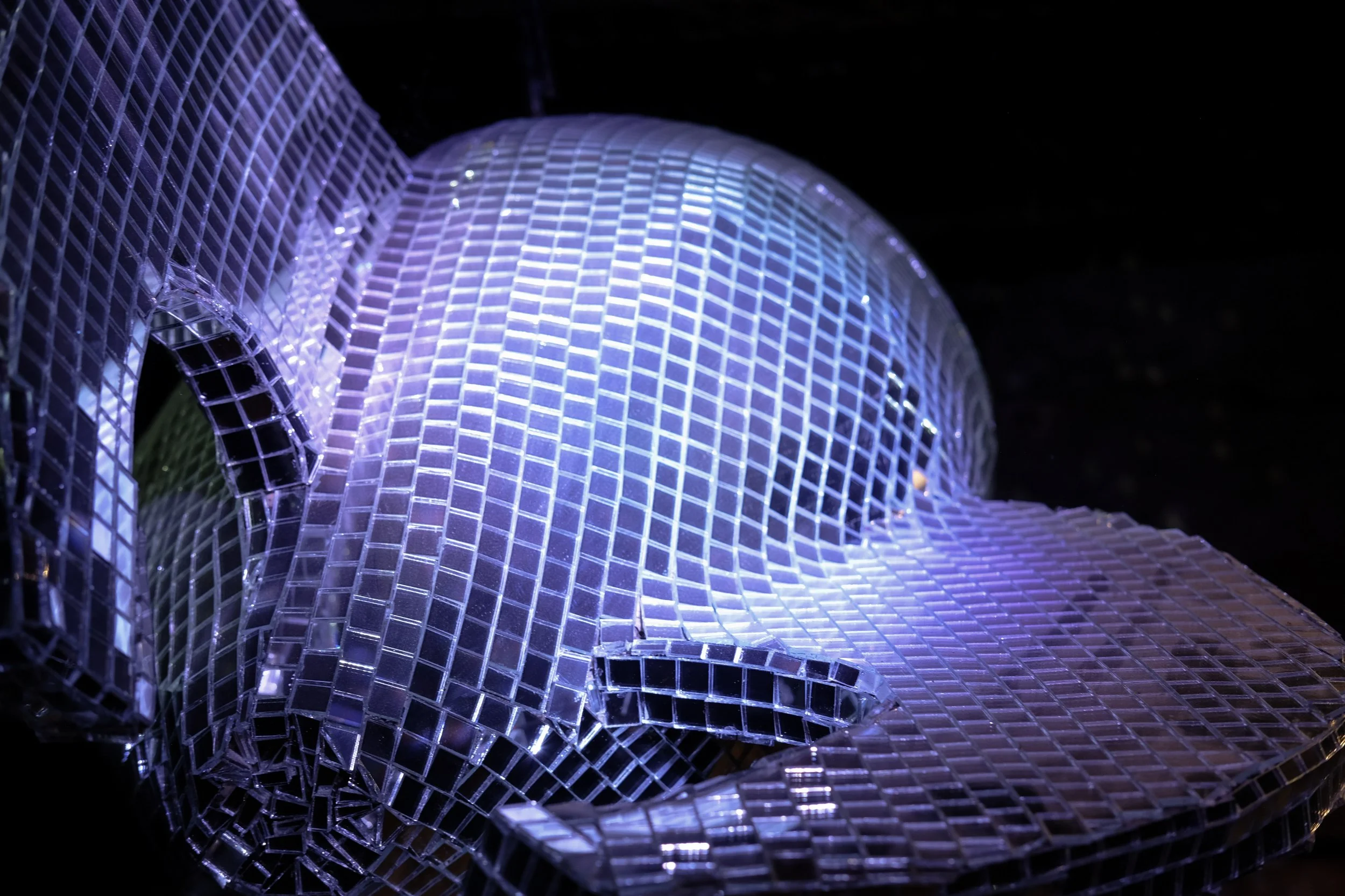 Close-up of illuminated, translucent, purple-tinted, geometric-shaped glass or acrylic sculptures with grid patterns, set against a dark background.