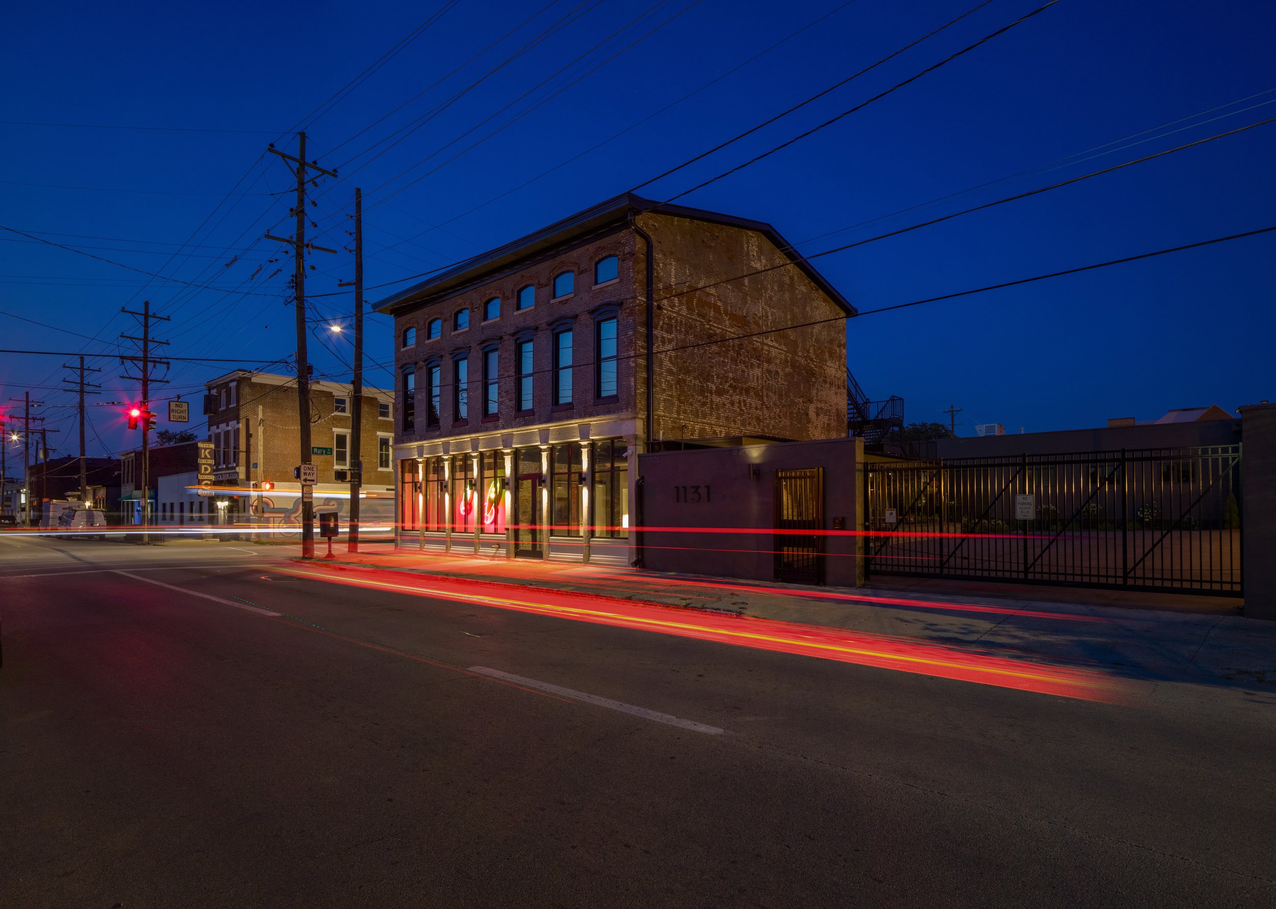 Nighttime street scene with historic brick building, power lines, traffic lights, and vehicle light trails.