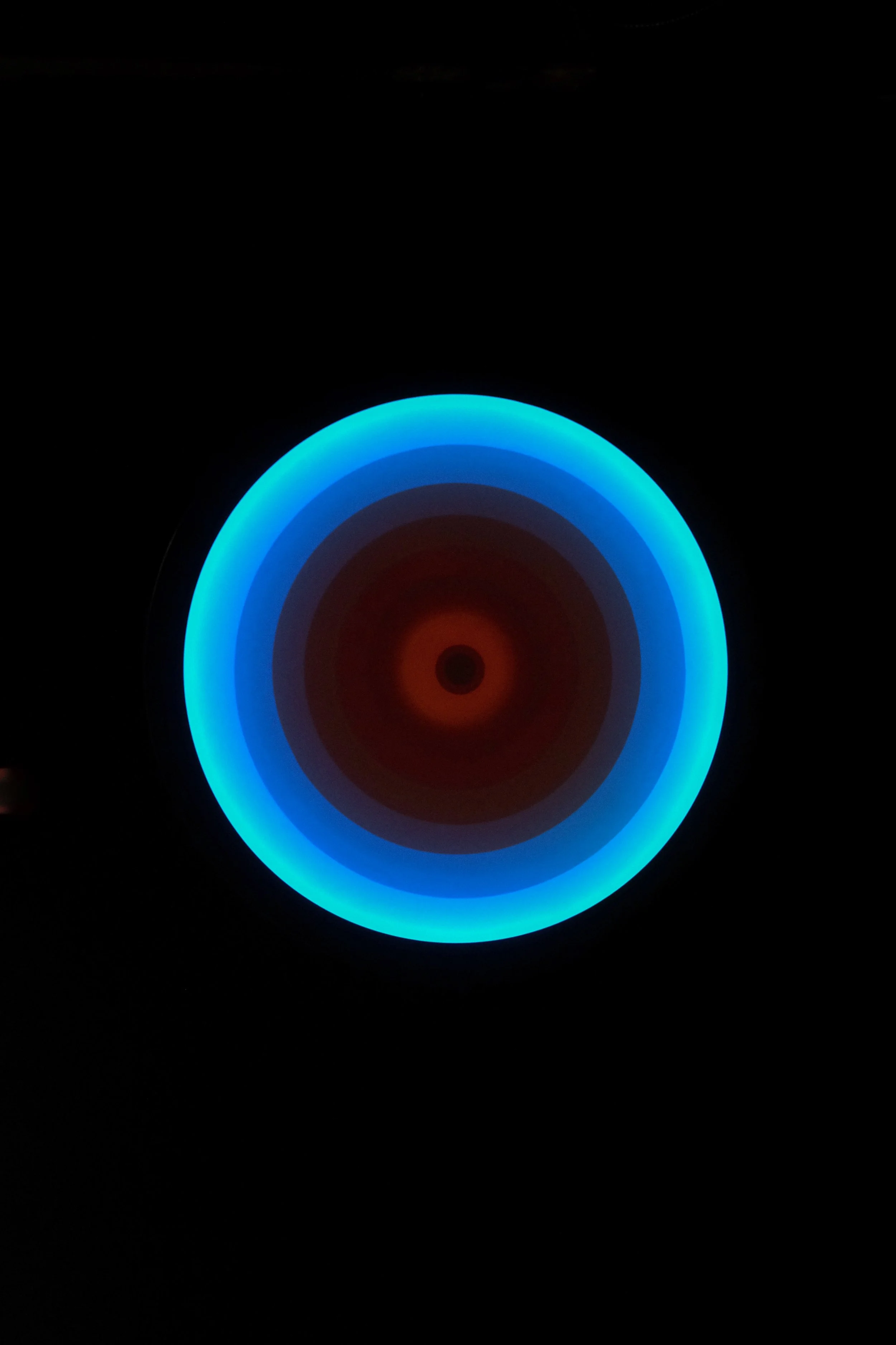 Close-up of a glowing, circular, multicolored LED light with blue, cyan, and red hues against a dark background.