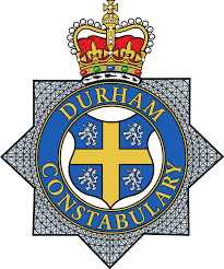 Badge of Durham Constabulary featuring a blue circle with a gold cross, four lions, and a crown on top.