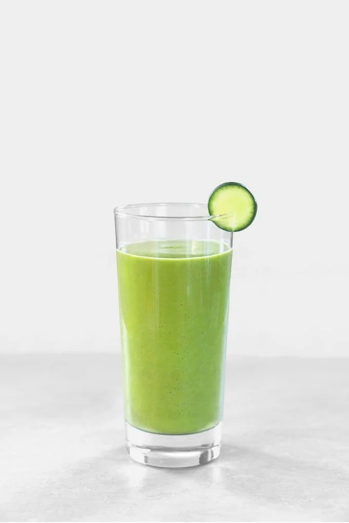A tall glass filled with green smoothie, garnished with a cucumber slice on the rim.